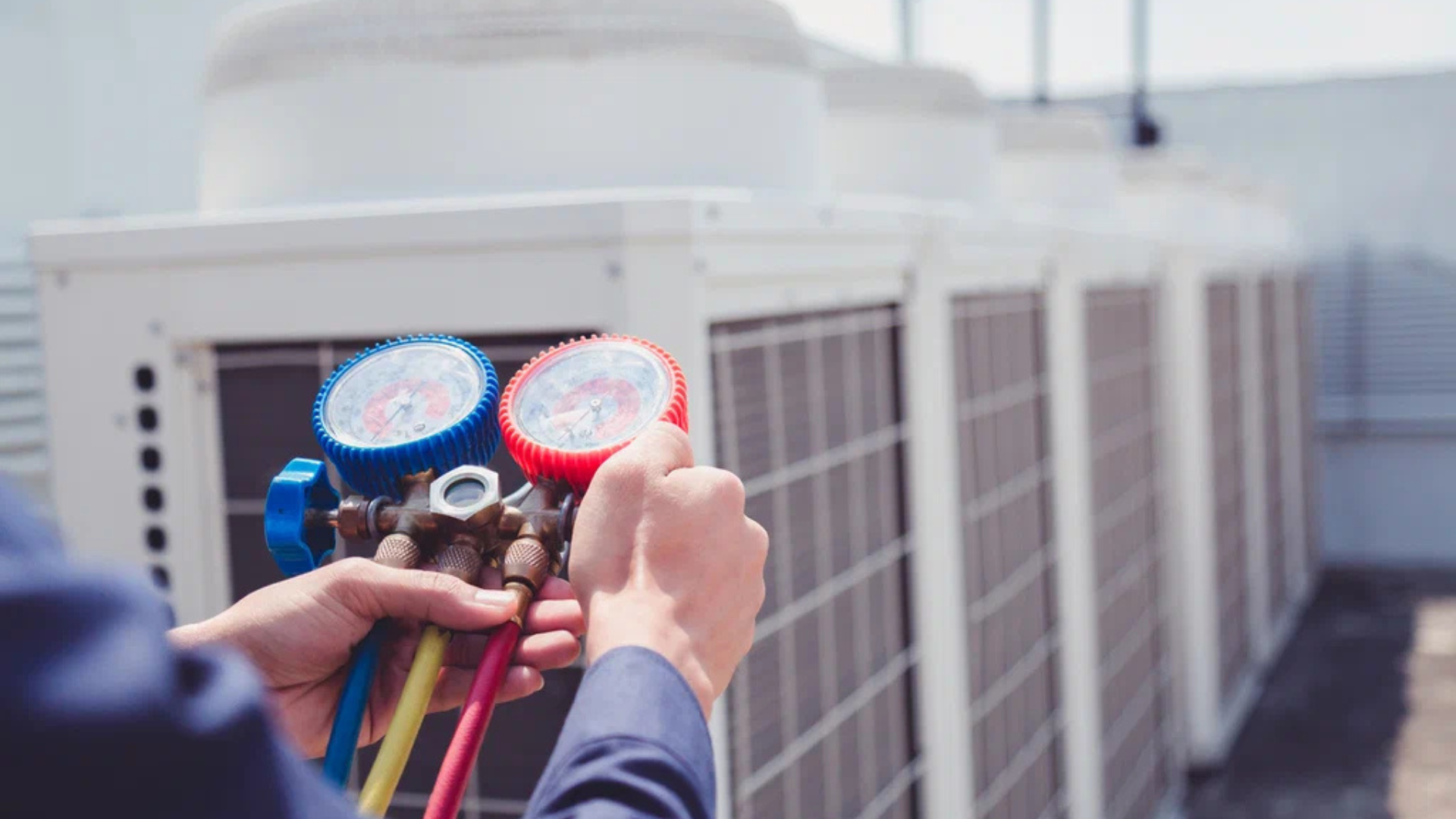 HVAC technician using gauges to check an air conditioning unit on a rooftop.