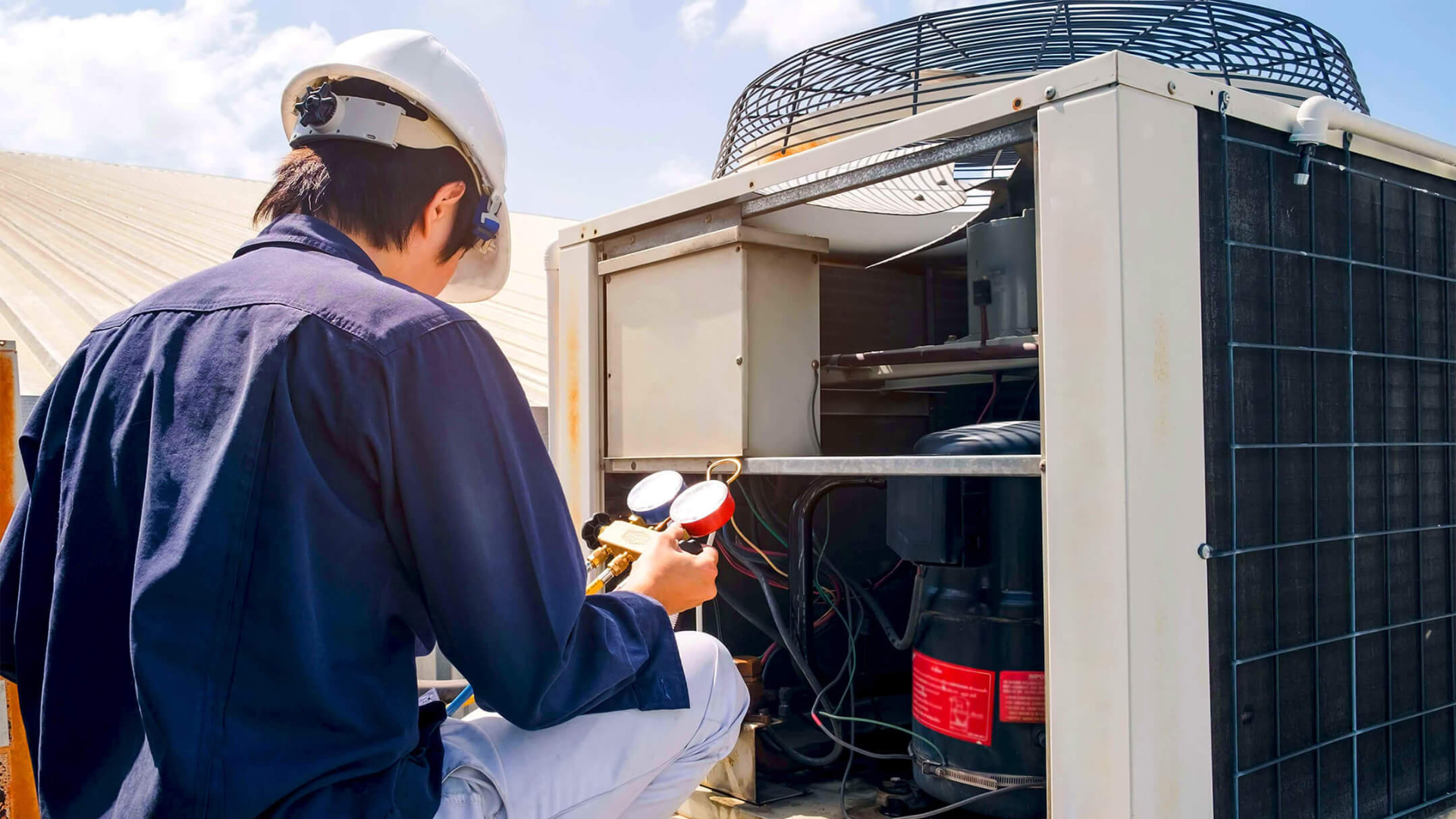 HVAC technician in hardhat, checking air conditioner on a rooftop.