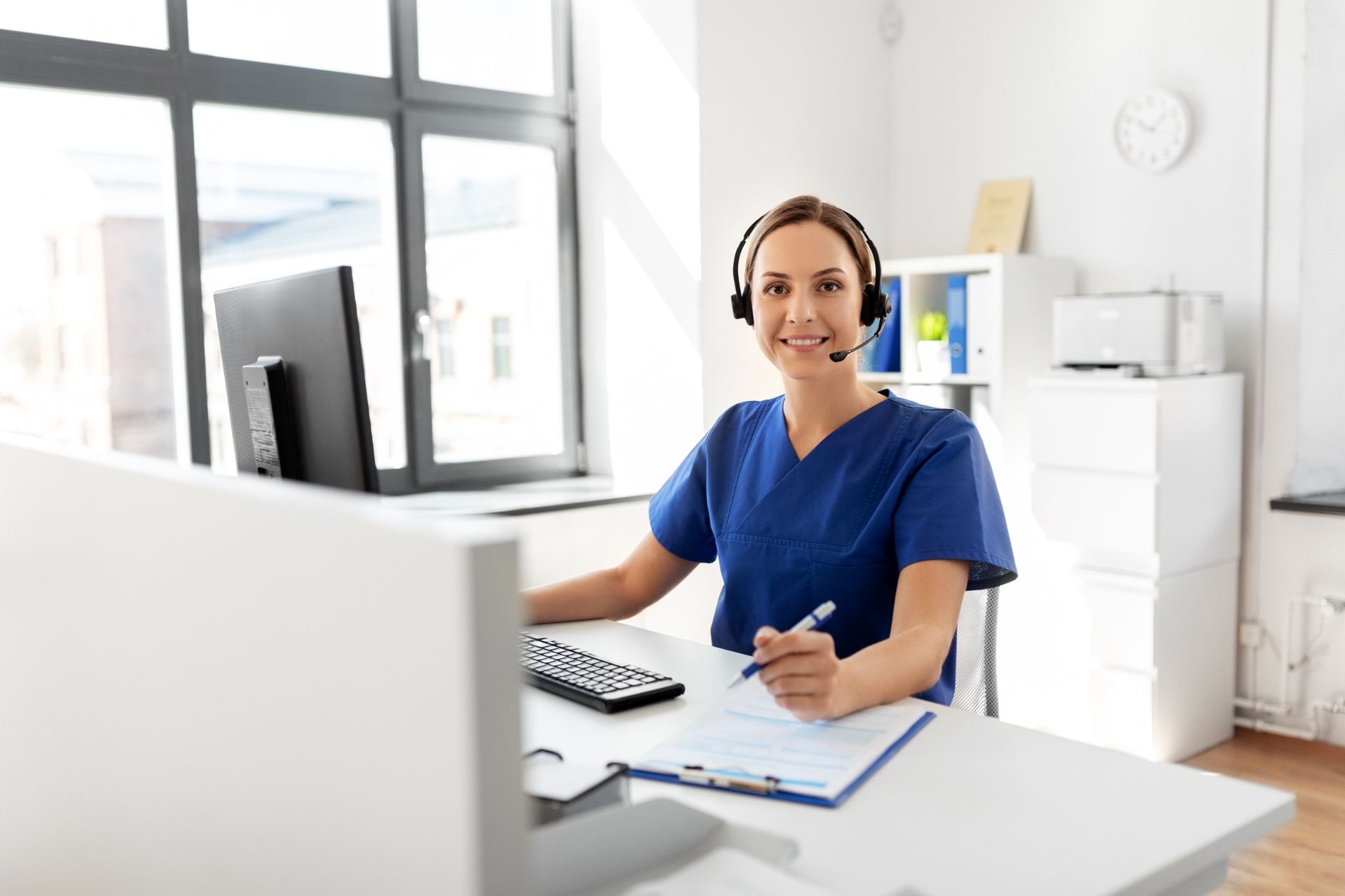 Female care coordinator in scrubs and headset assisting patients through a remote monitoring platform.