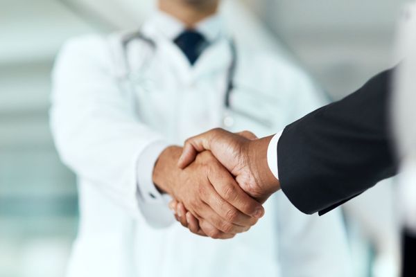 Close-up of a physician shaking hands with a healthcare business partner, symbolizing a Remote Patient Monitoring partnership.