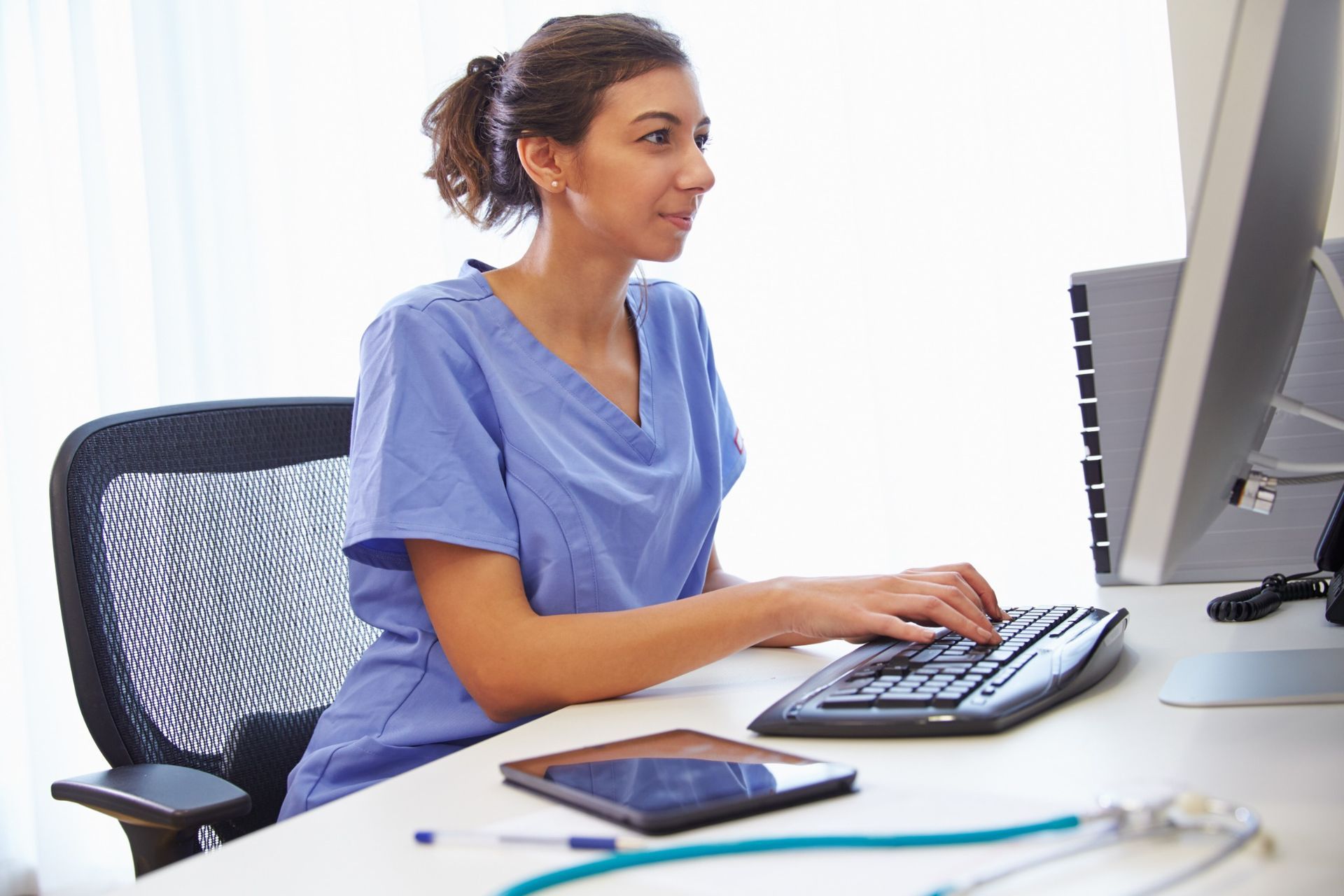 Nurse documenting a patient care plan at a computer workstation, showcasing clinical efficiency in chronic care management.