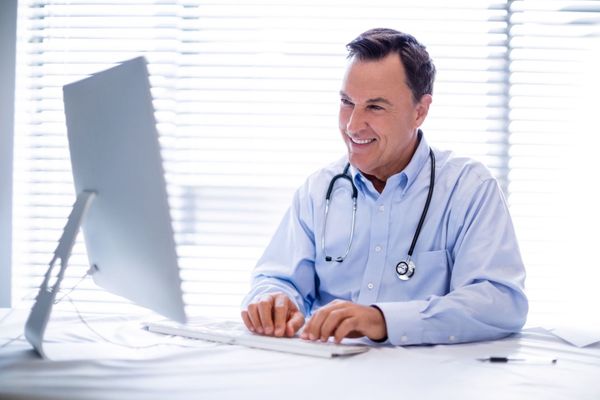 Doctor smiling while reviewing remote patient data on a computer, highlighting the benefits of RPM services.