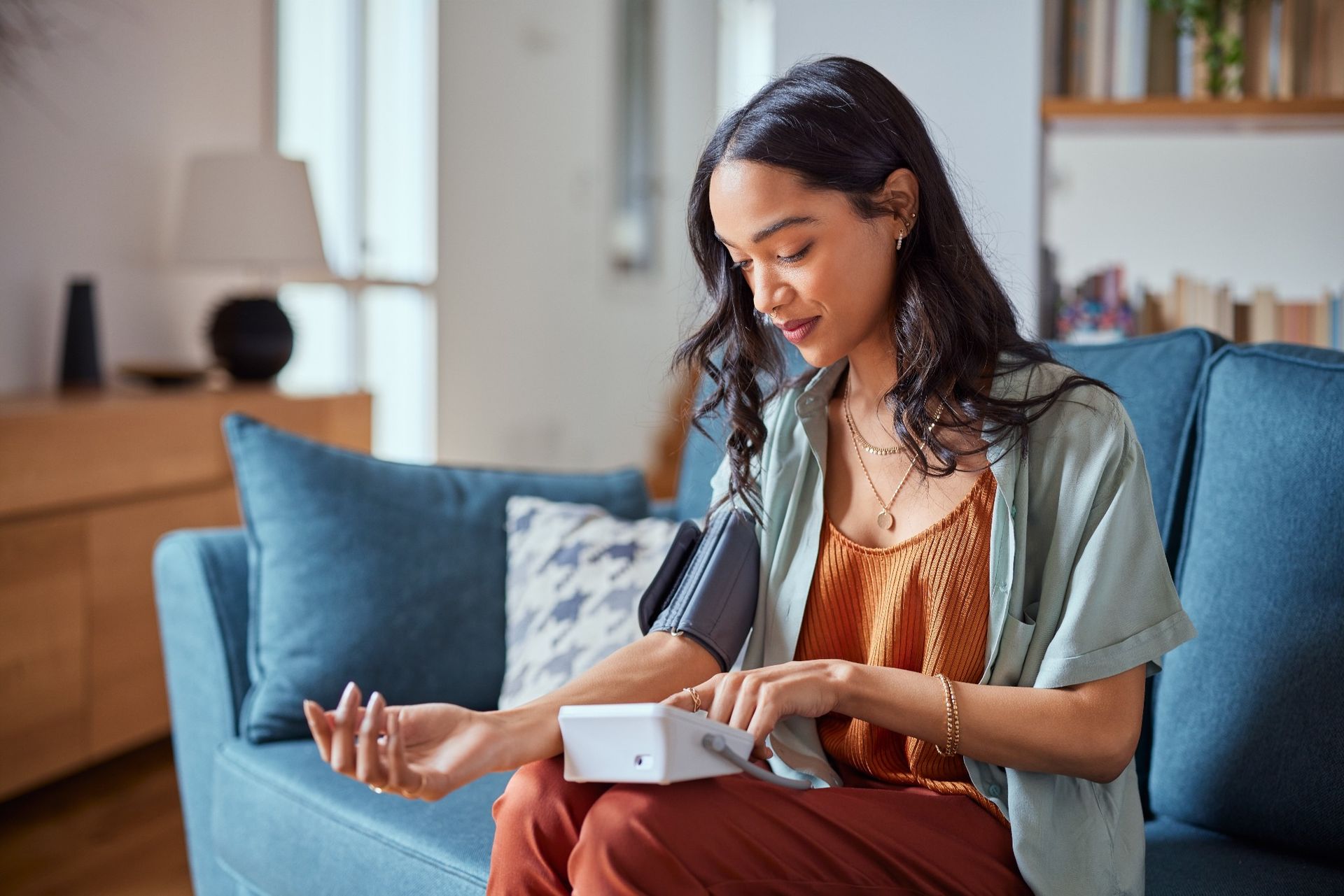 Young woman comfortably seated while checking her blood pressure with a home monitoring device.