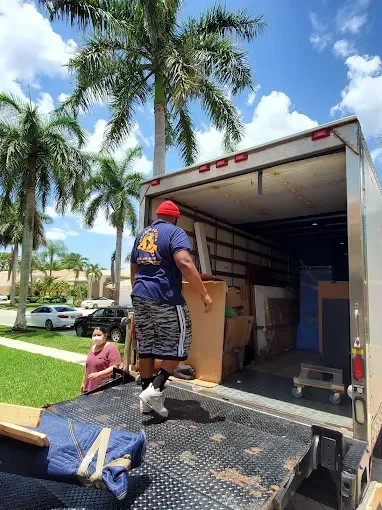 A person loads a moving truck with boxes and furniture outdoors on a sunny day.