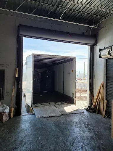 A box truck is backed into a warehouse bay. The open bay door reveals the cargo area.