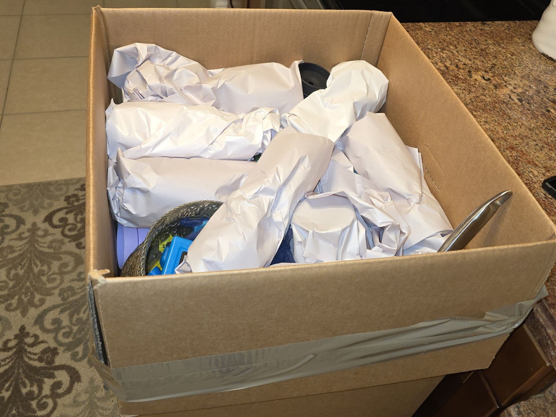 Cardboard box filled with items wrapped in white paper, possibly for shipping.