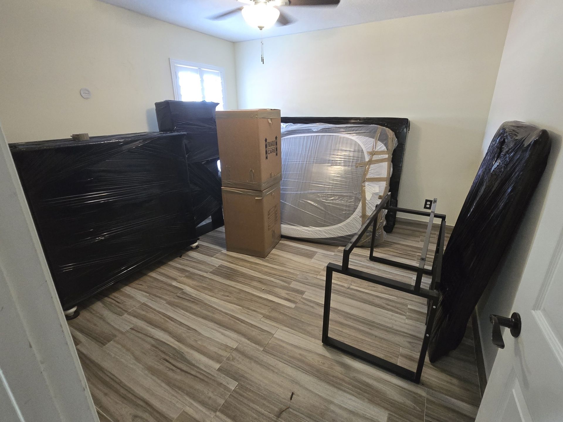 Room with furniture wrapped for moving, including a bed, dresser, and boxes.