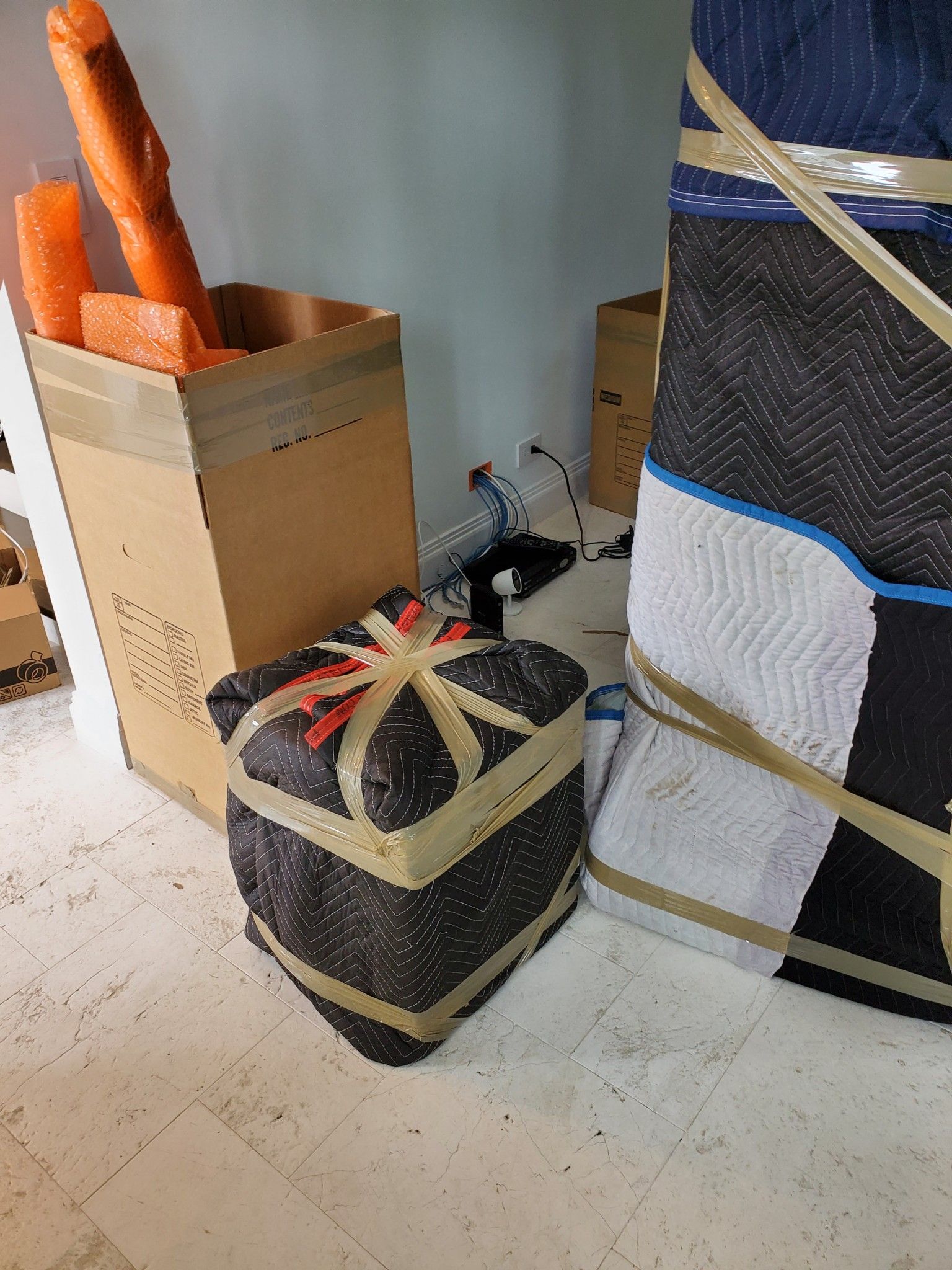 Cardboard boxes and wrapped parcels on a white floor. One parcel is gift-wrapped with tape.