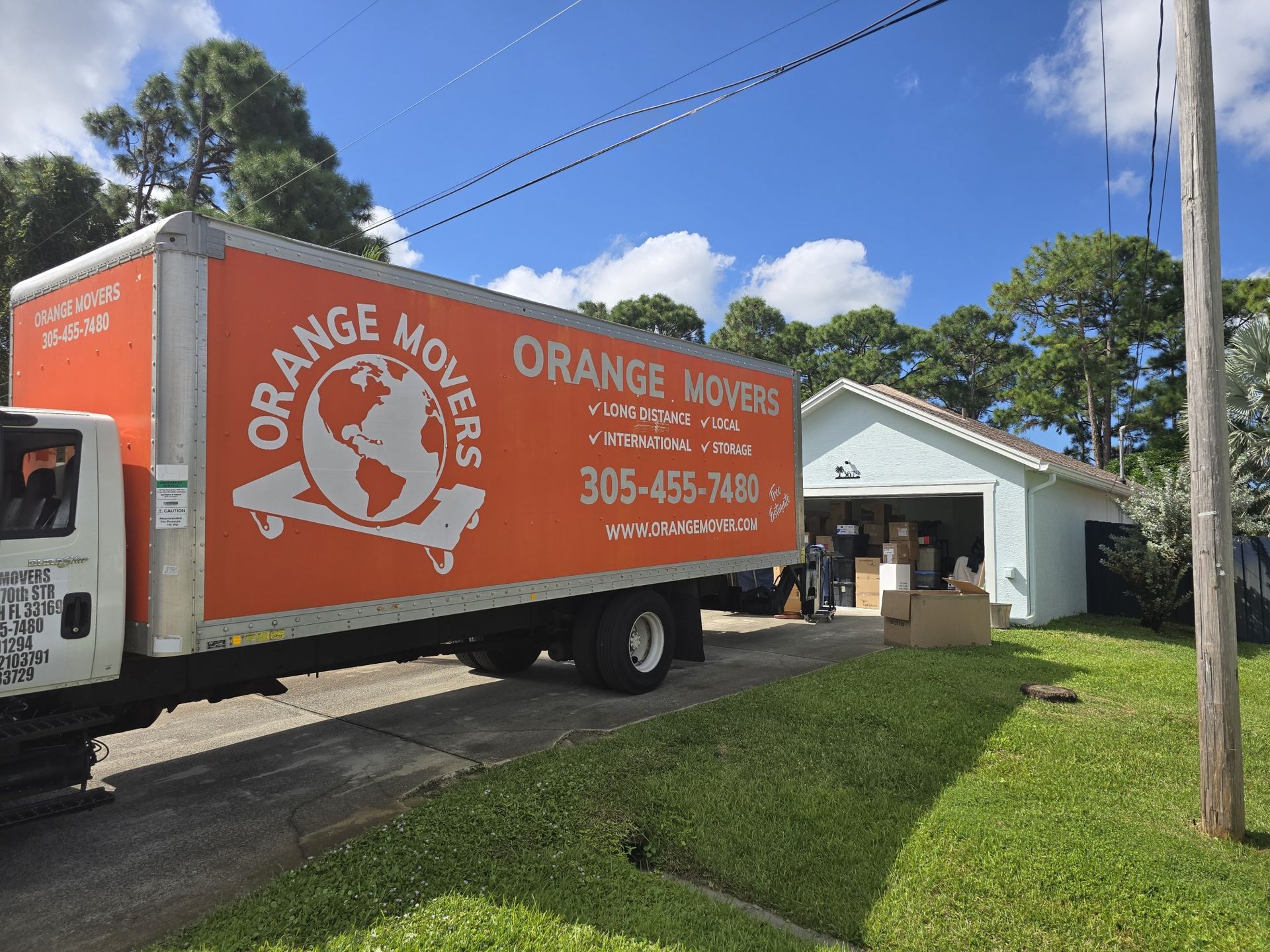 Orange movers truck parked, boxes in garage, people moving.