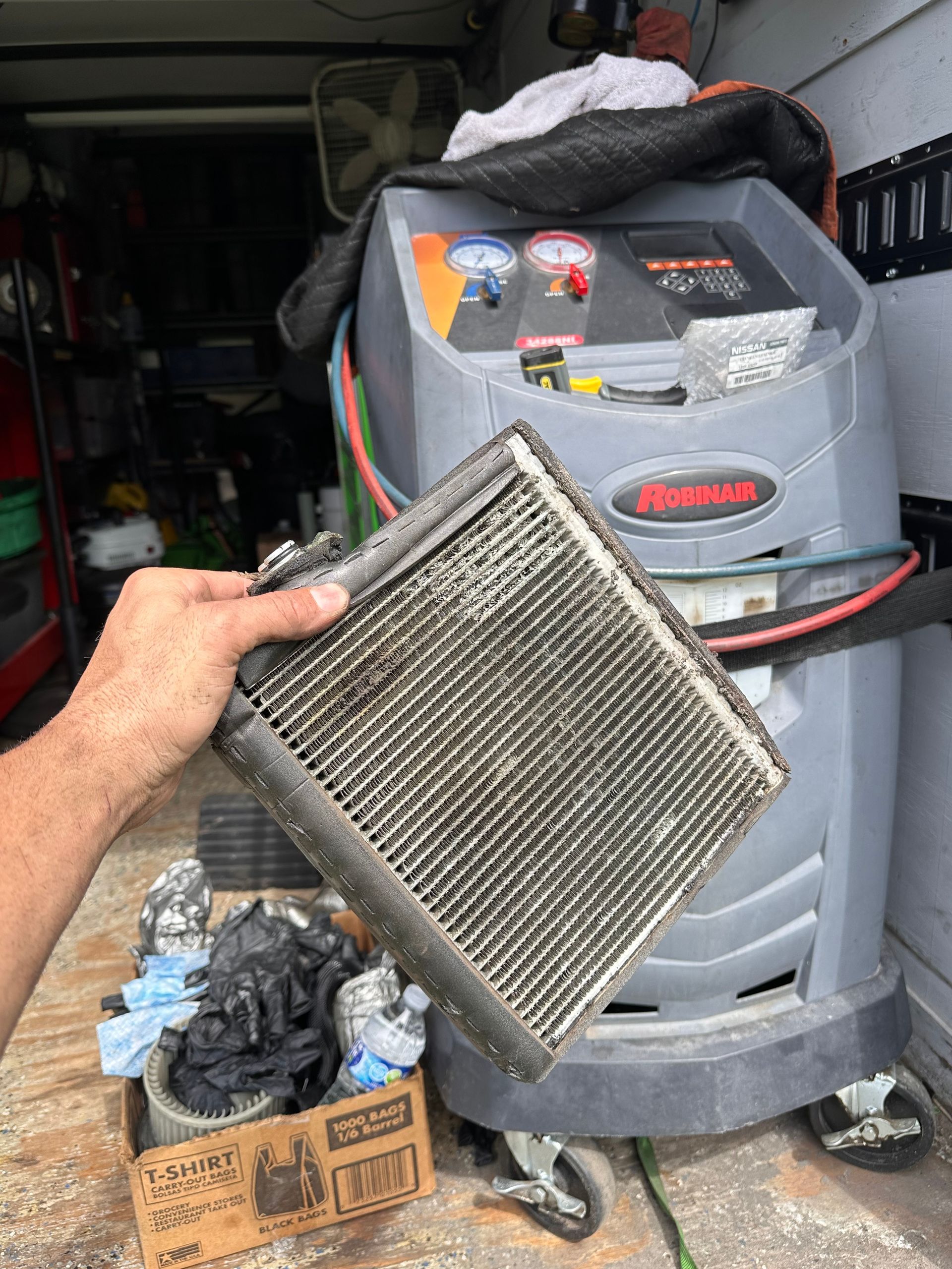 Hand holding a dirty, rectangular air conditioning evaporator coil | 3T’s Mobile Automotive Repair Inc.