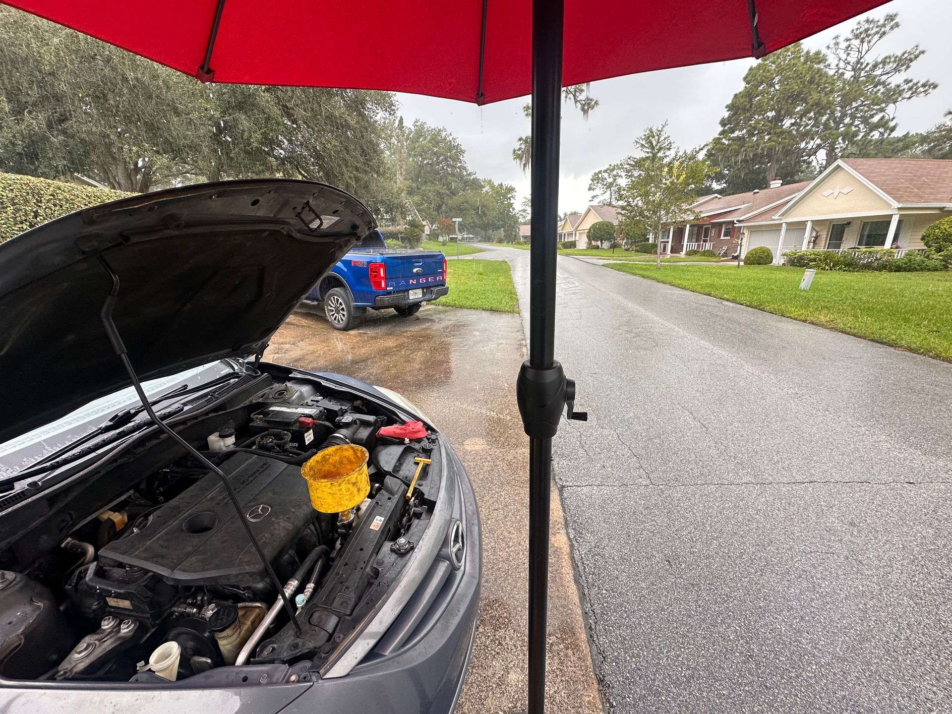 Car with open hood under a red umbrella | 3T’s Mobile Automotive Repair Inc.