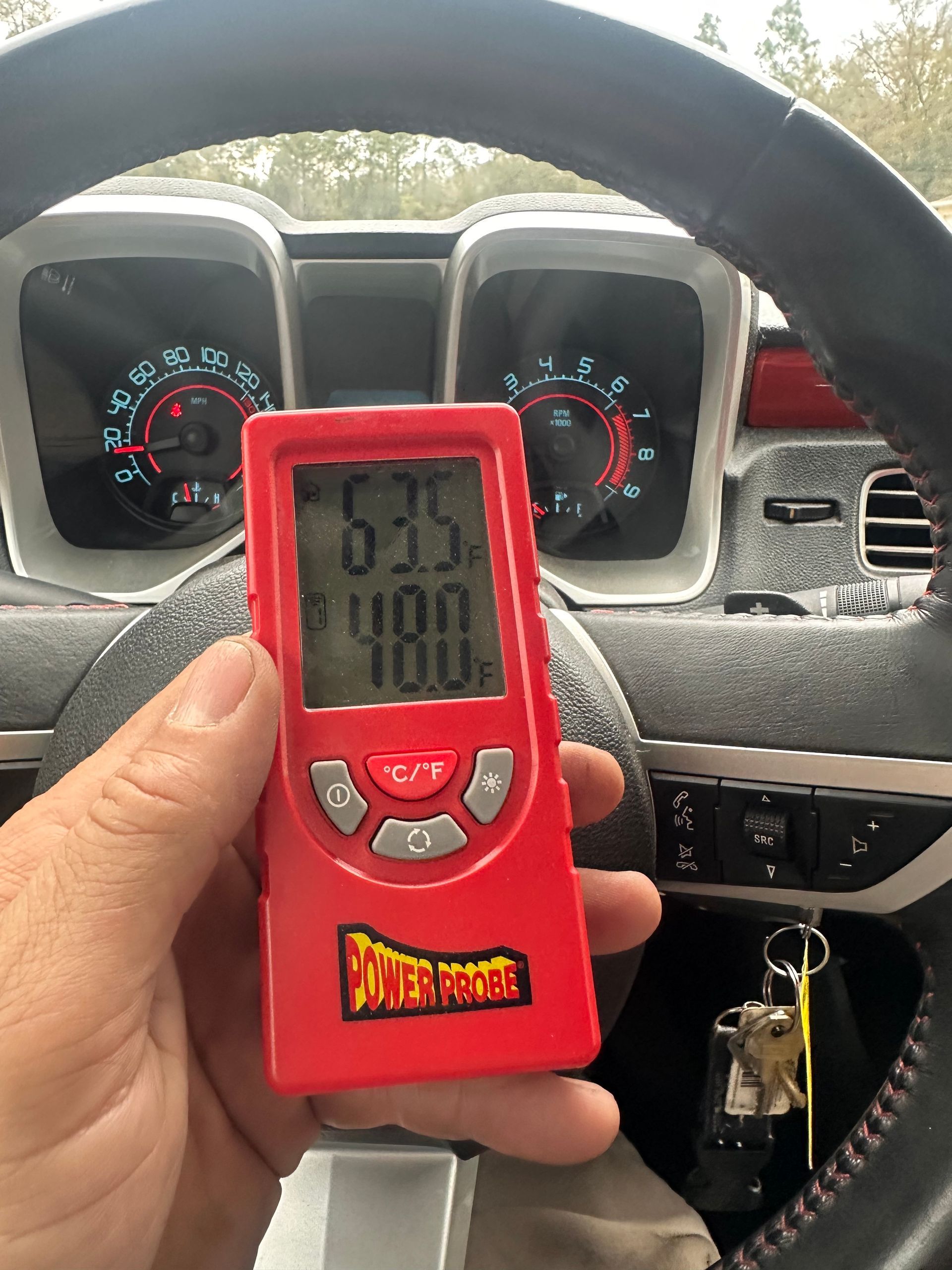 A hand holding a red thermometer in a car | 3T’s Mobile Automotive Repair Inc.