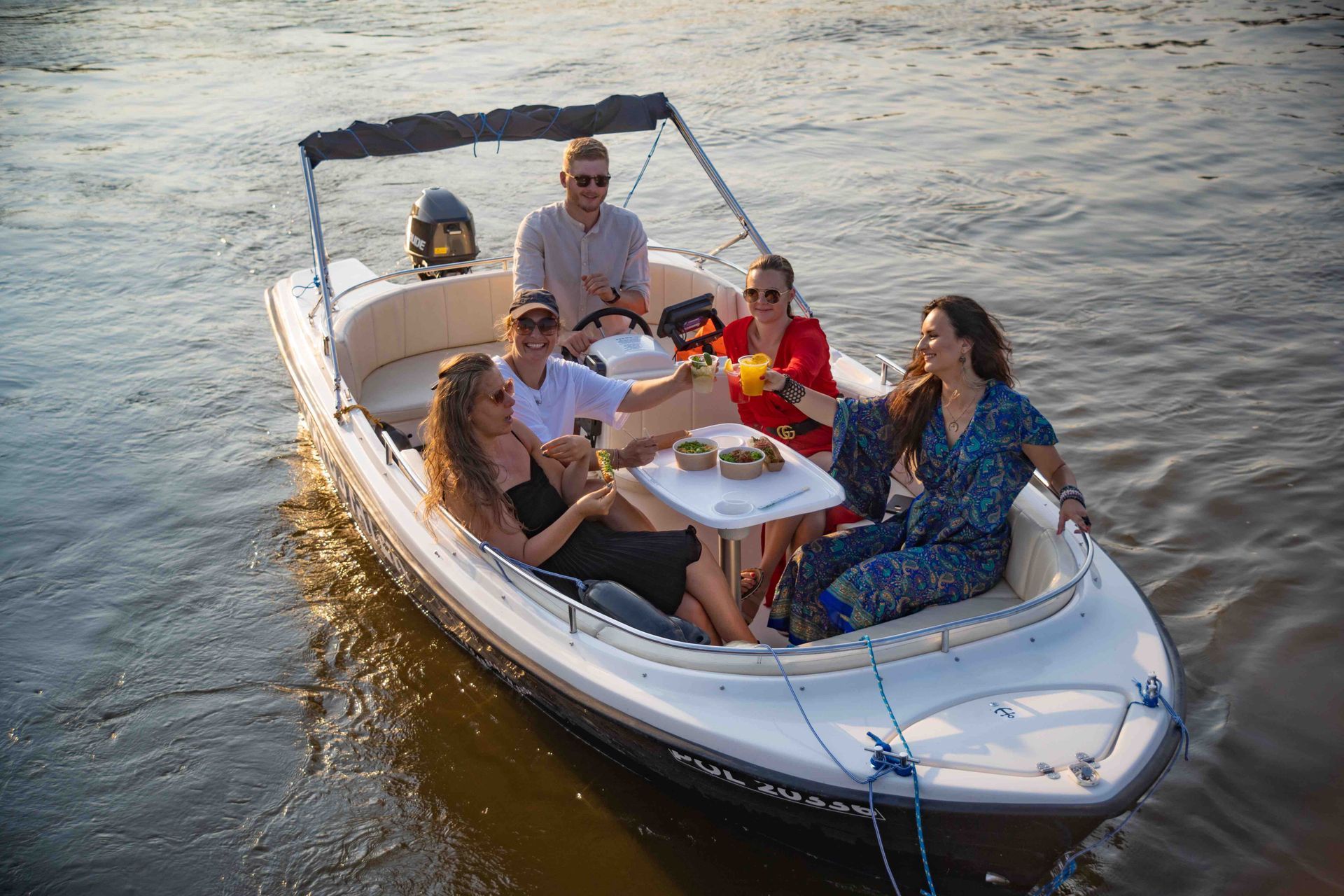 Zespół przyjaciół cieszący się posiłkiem i napojami na pokładzie 5 osobowej łodzi motorowej w Warszawie