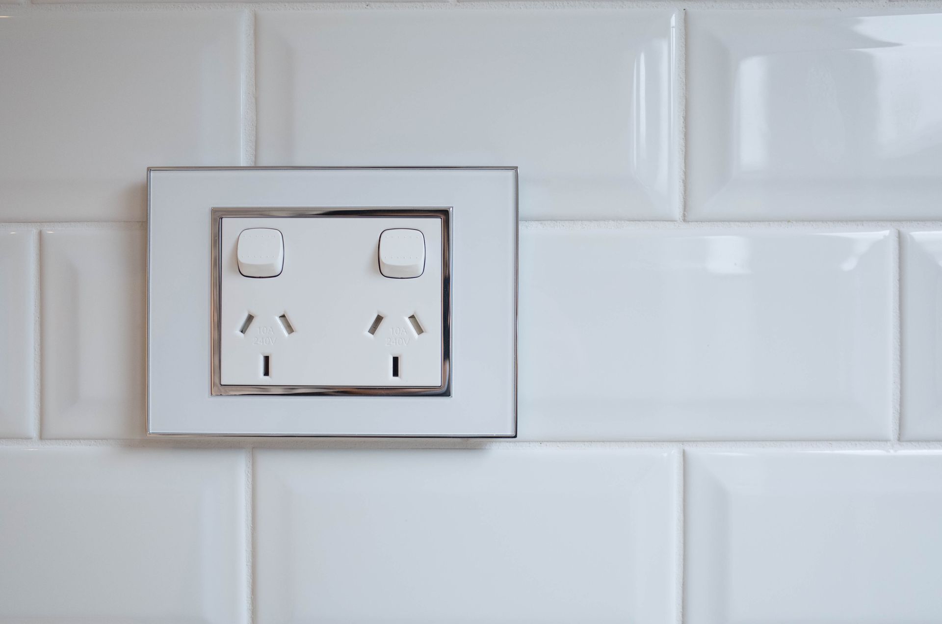A double Australian power outlet installed on a white tiled wall.