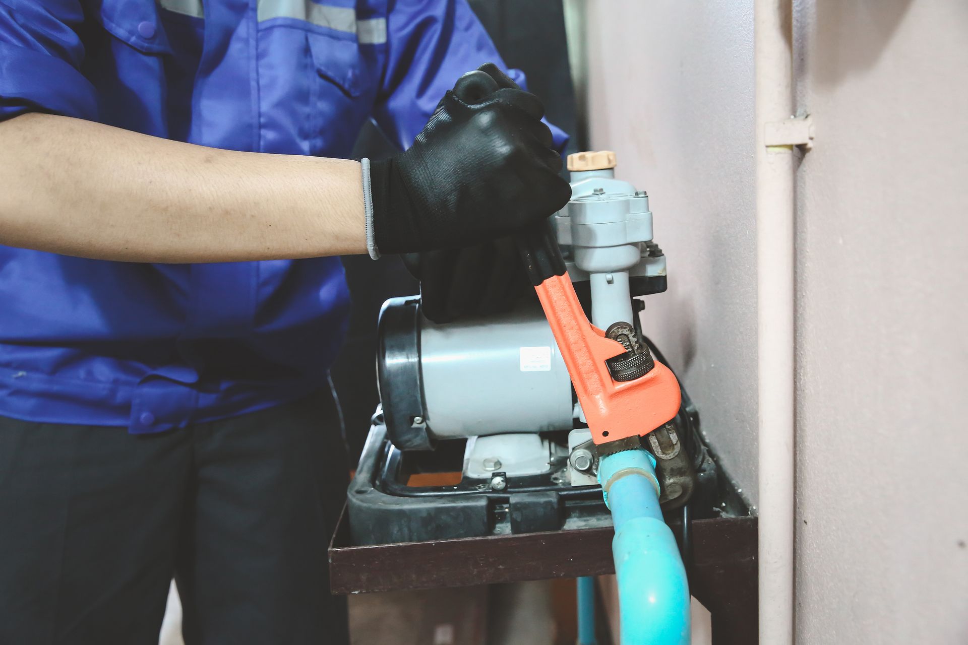 Person in blue uniform adjusts a water pump, wearing black gloves.