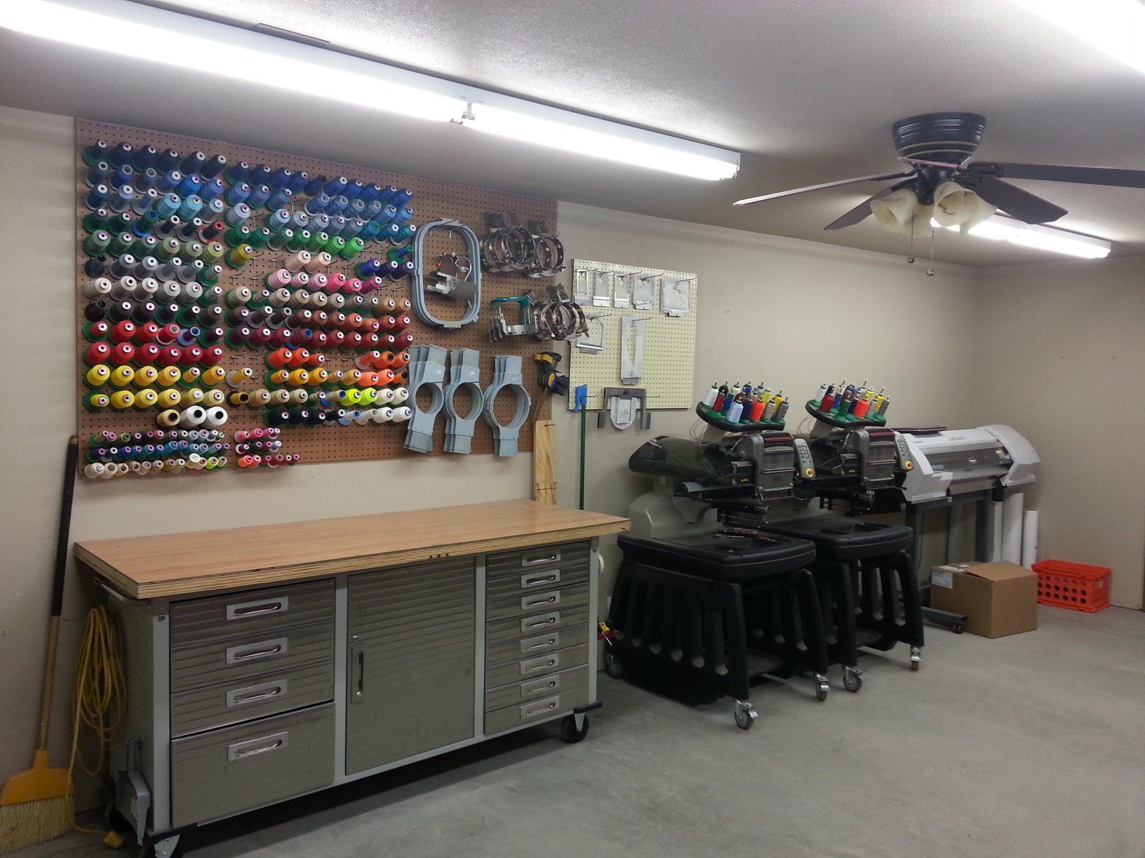 wall of colorful embroidery thread options, two embroidery machines and vinyl graphics applicator