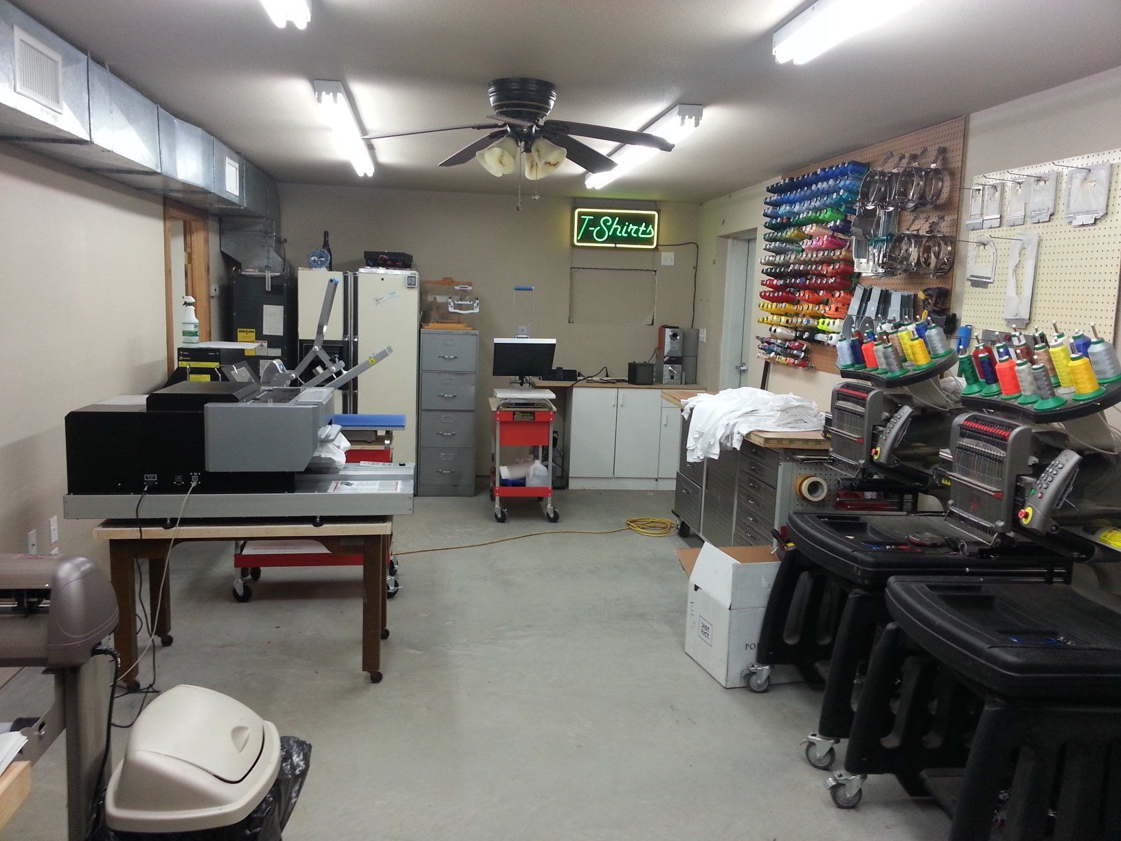 alternate view of studio featuring colorful embroidery threads, two embroidery machines and screen printing machine
