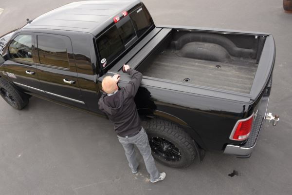 aerial view of man opening retractable truck bed cover on black four door pickup truck