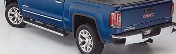 rear angle view of blue GMC Sierra pickup truck with full running board