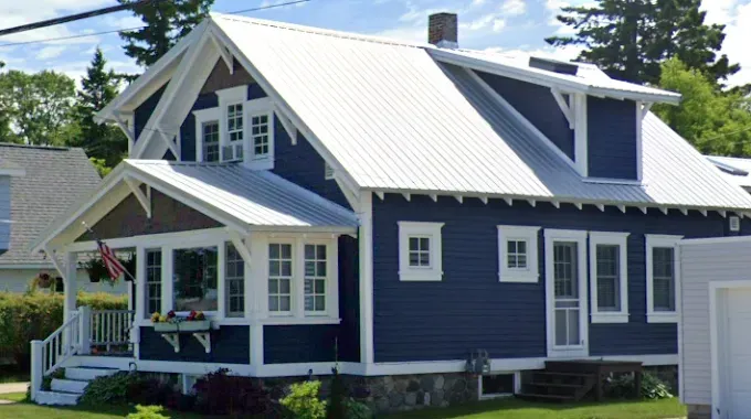White two-story house with black shutters and a black roof on a sunny day.