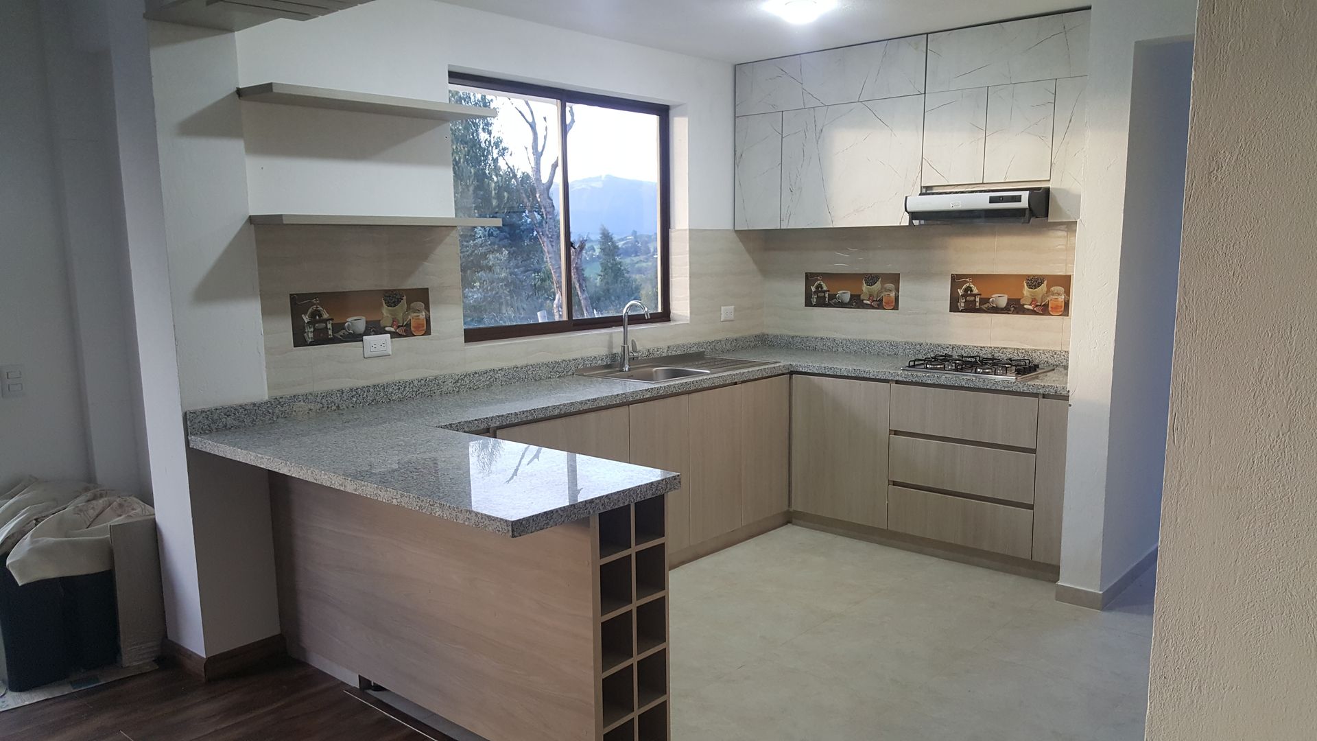 Cocina moderna con gabinetes de madera clara, encimeras de granito y barra de desayuno.