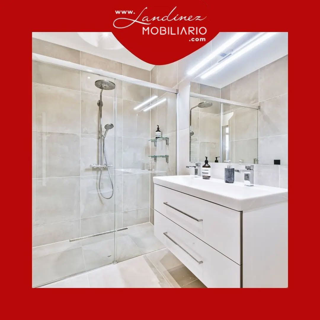 Baño moderno con ducha de cristal, tocador blanco y azulejos de colores neutros.