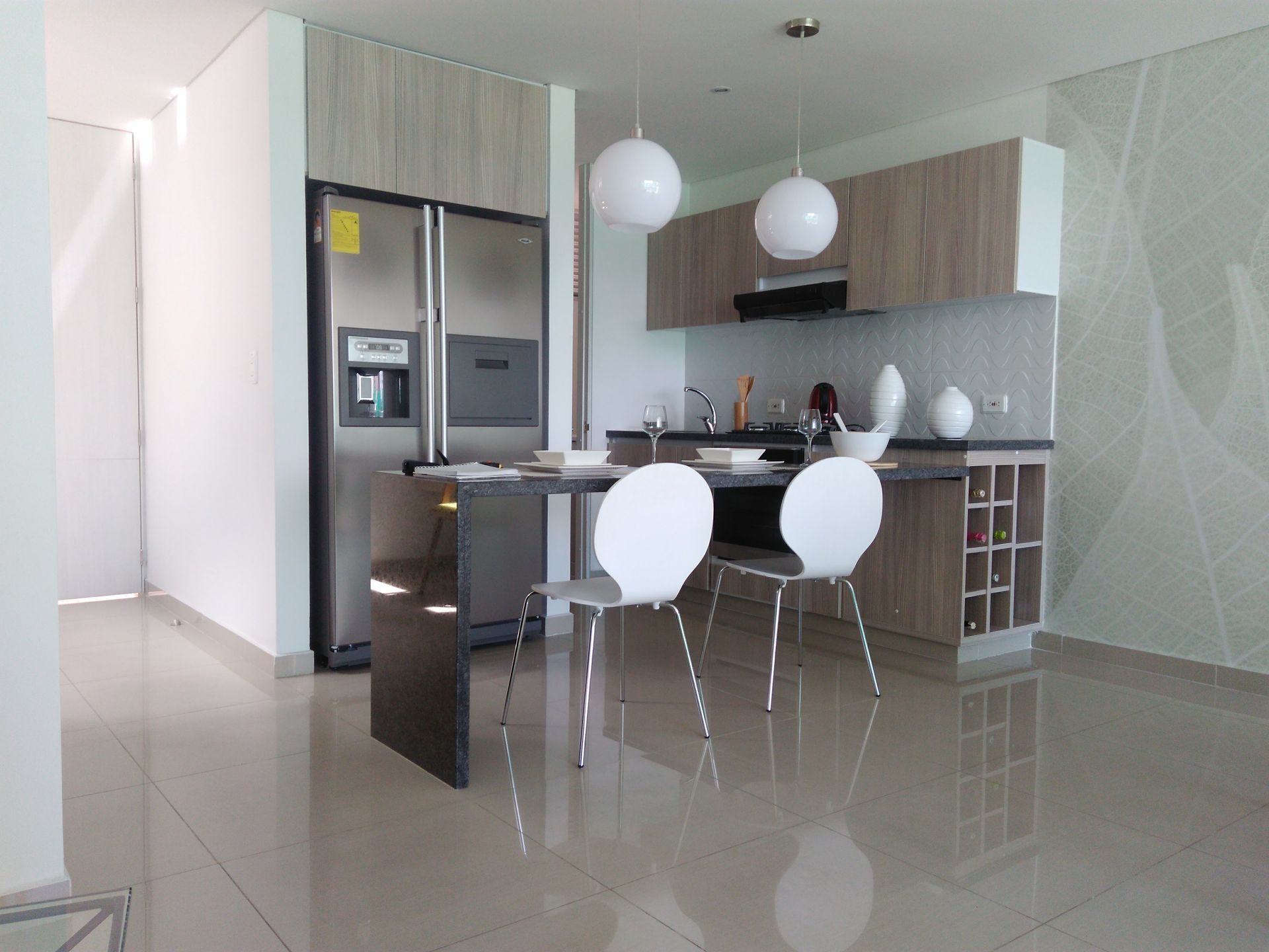 Cocina moderna con electrodomésticos de acero inoxidable, gabinetes de madera clara y comedor con sillas blancas.