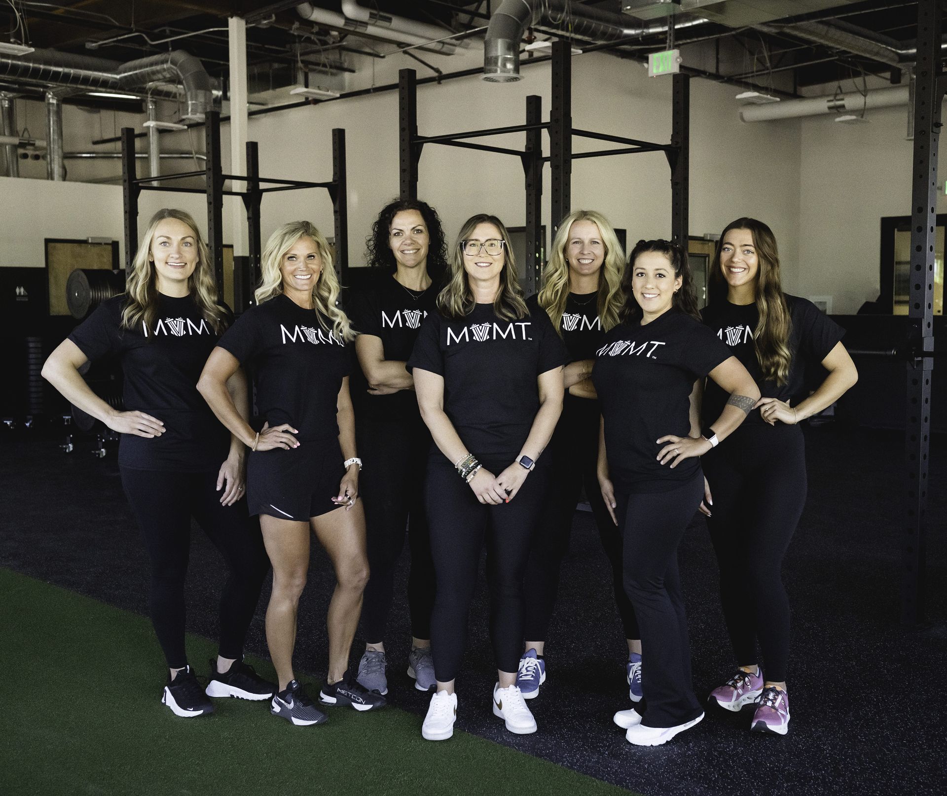 Group of seven people wearing black shirts and pants posing in a gym.