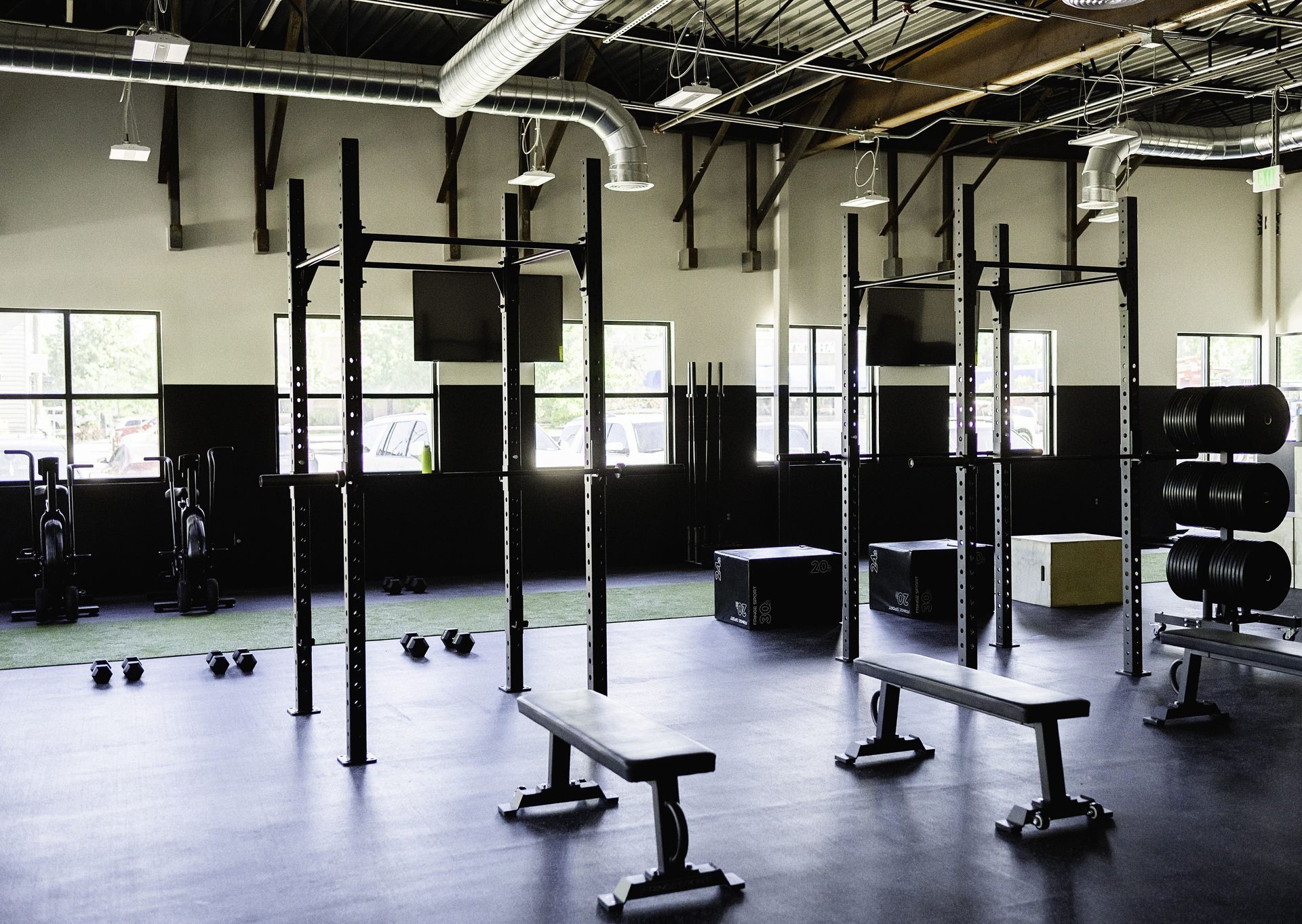 Gym interior with weightlifting equipment: pull-up bars, benches, dumbbells, and medicine balls.
