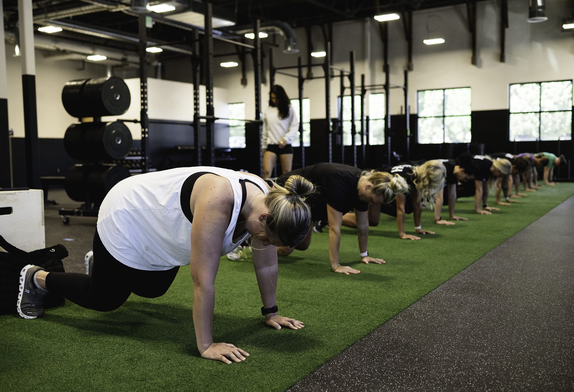 People in a gym performing plank exercises on artificial turf.