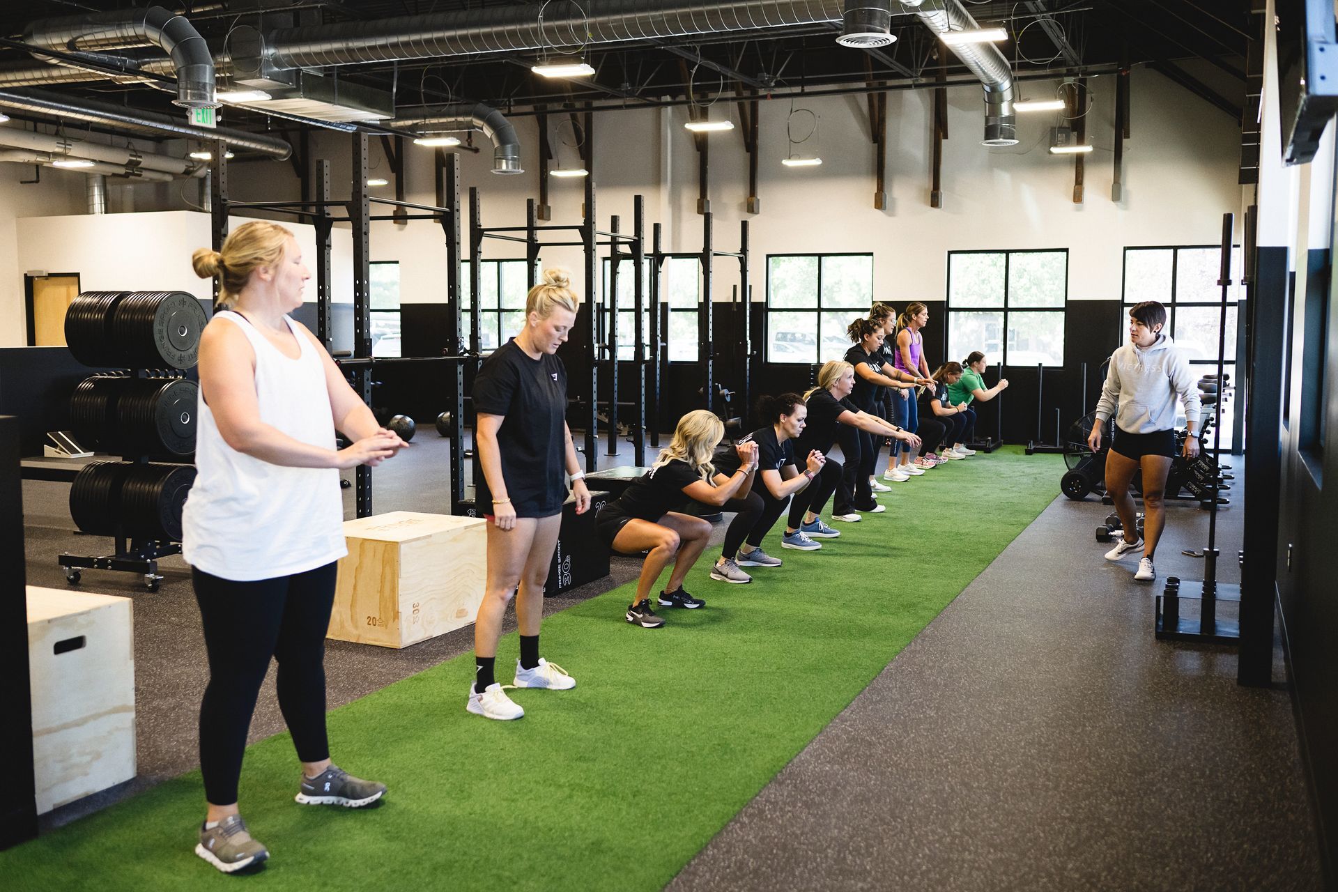 People exercising in a gym; instructor watches as group does squats on artificial turf.