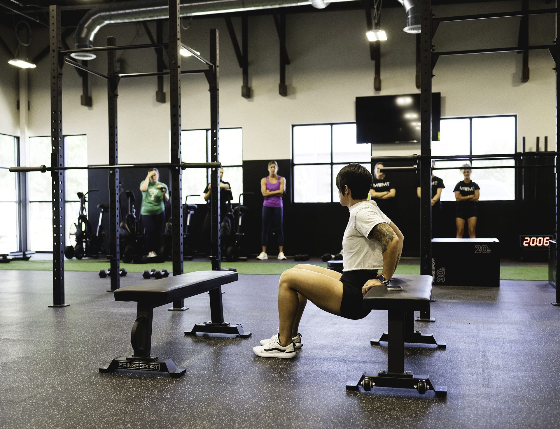 Woman doing bench dips in a gym, with other people in the background.