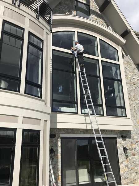 A man on a ladder is cleaning the windows of a large house.
