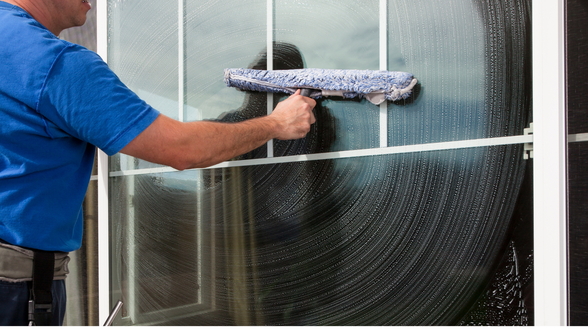 A man in a blue shirt is cleaning a window with a squeegee.
