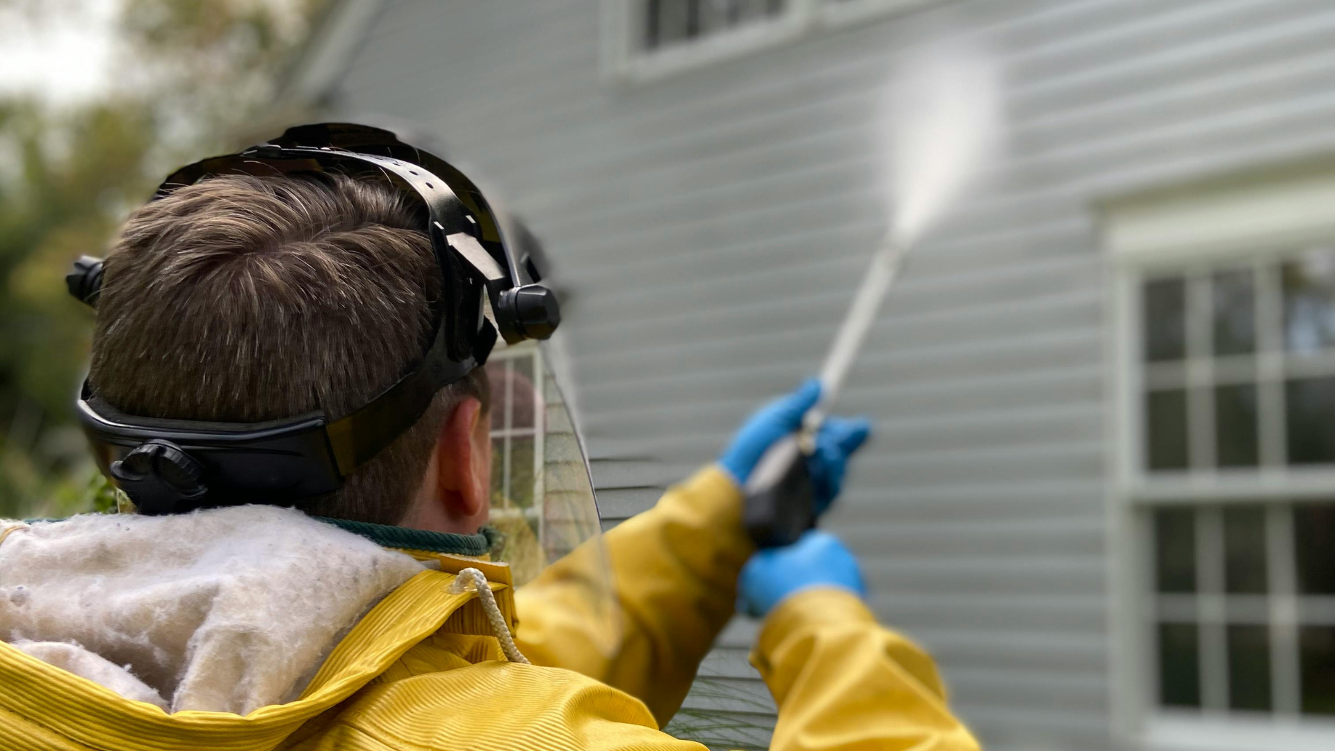 A man is cleaning the side of a house with a high pressure washer.