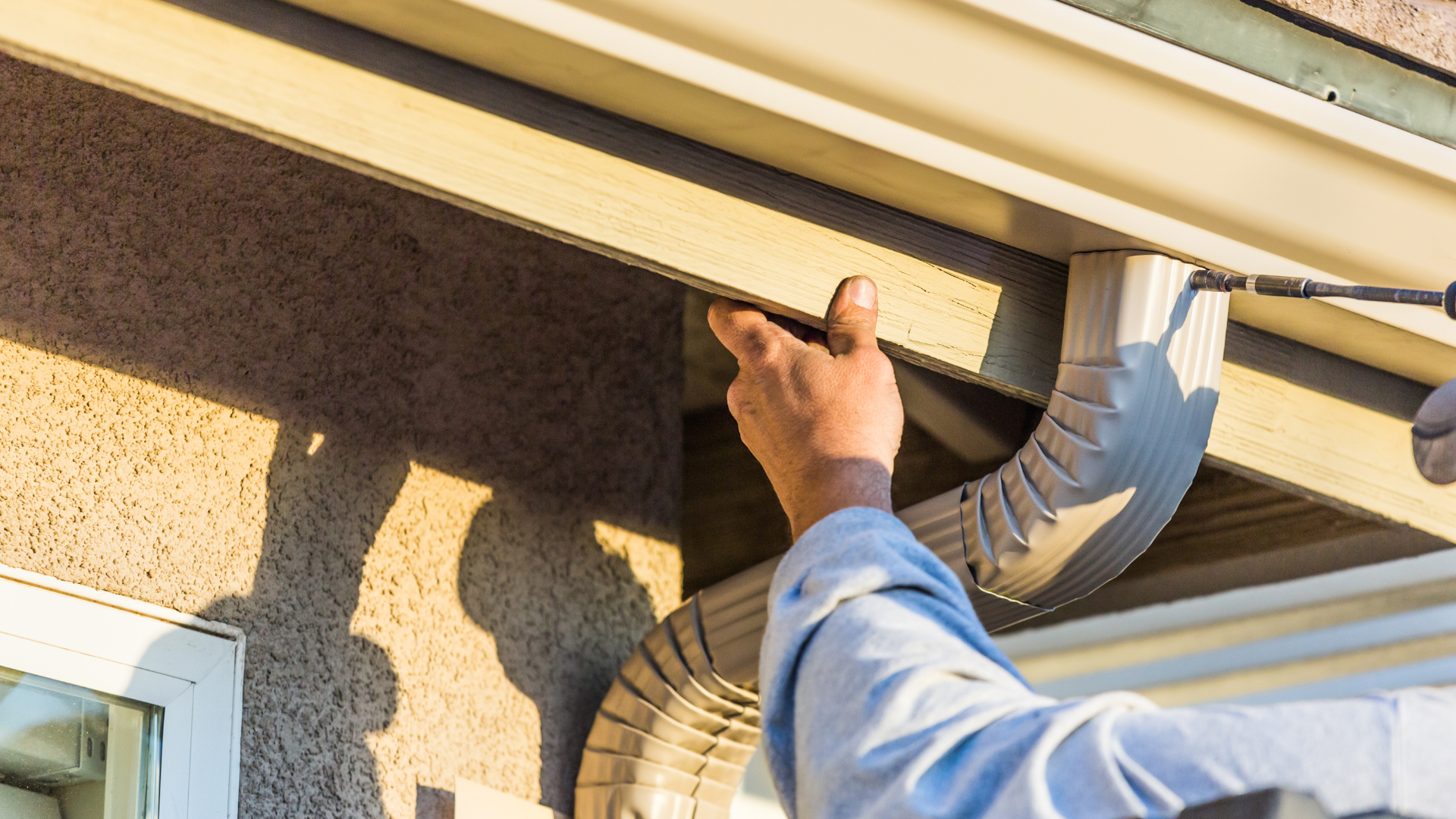 A man is fixing a gutter on the side of a house.