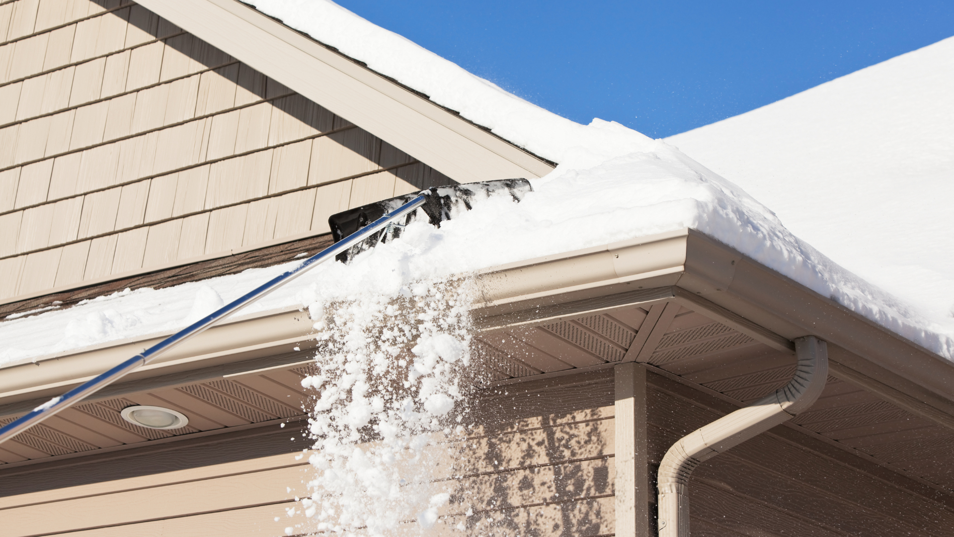 A person is clearing snow from the roof of a house.