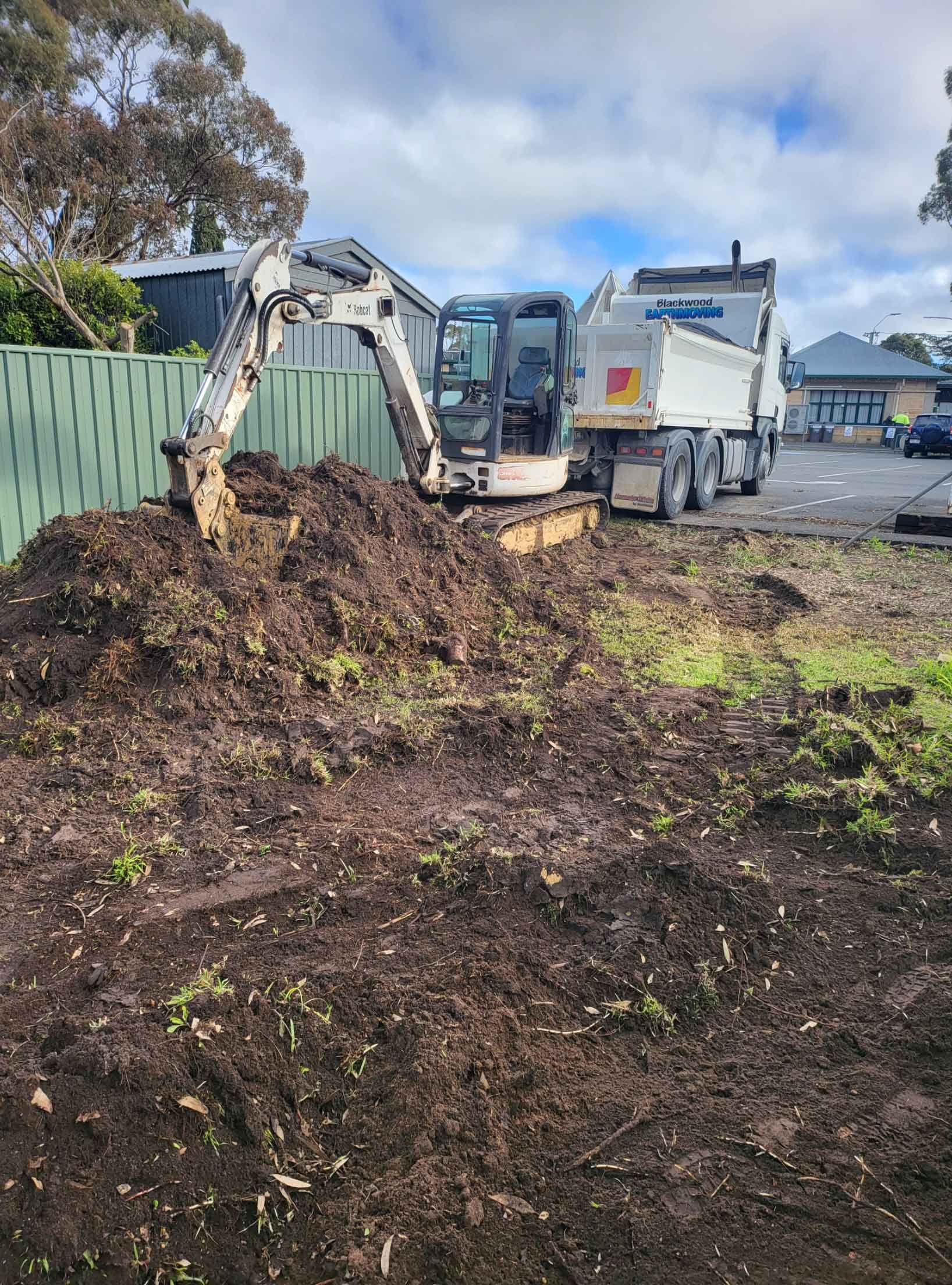 An Excavator Is Digging A Hole In A Yard Next To A Dump Truck – Blackwood SA - Blackwood Earthmoving