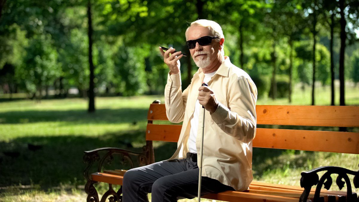 Rentner sitzt auf Parkbank und nutzt sein Smartphone über den Sprachassistenten