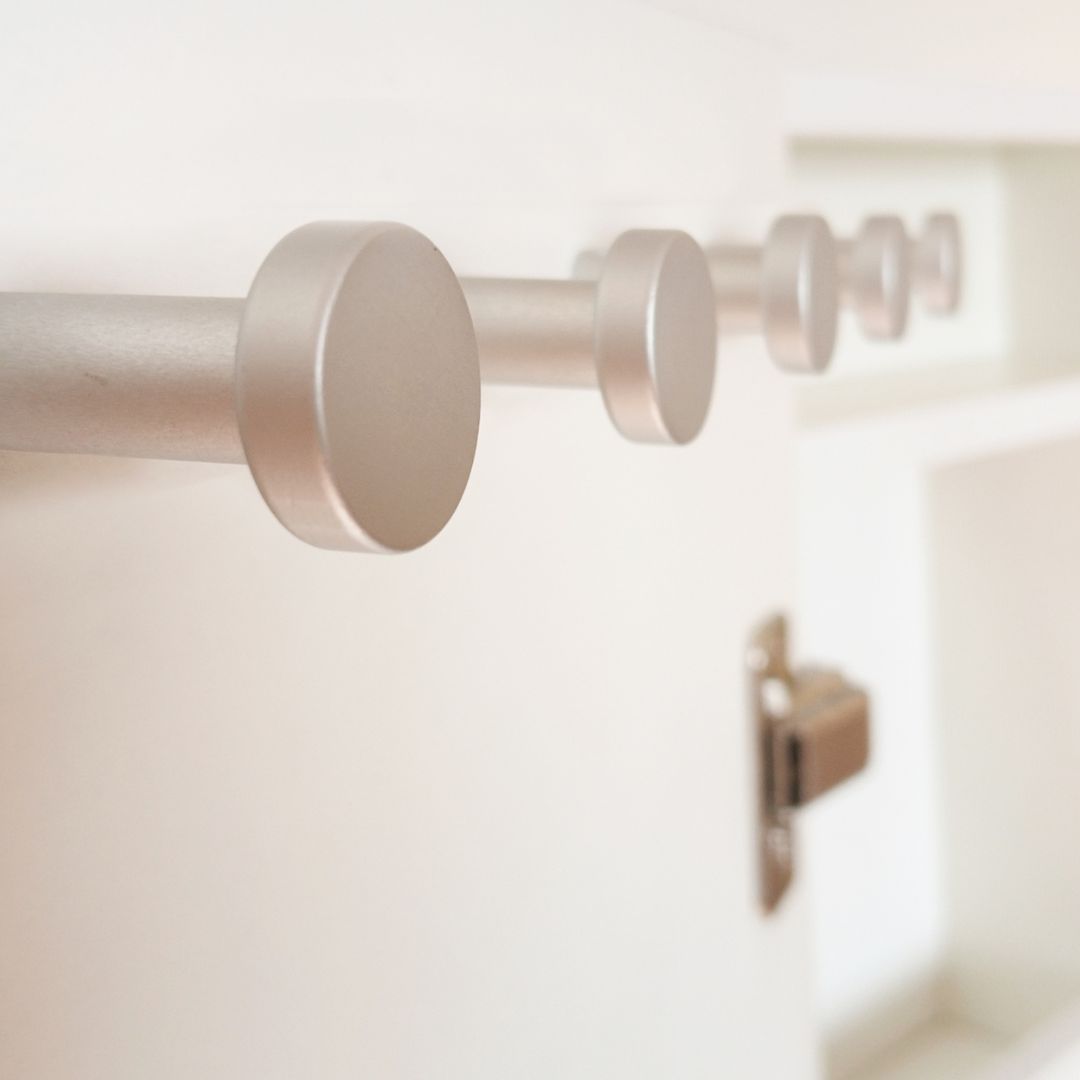 Primer plano de barras y soportes de cortina plateados en una pared blanca en una habitación luminosa.