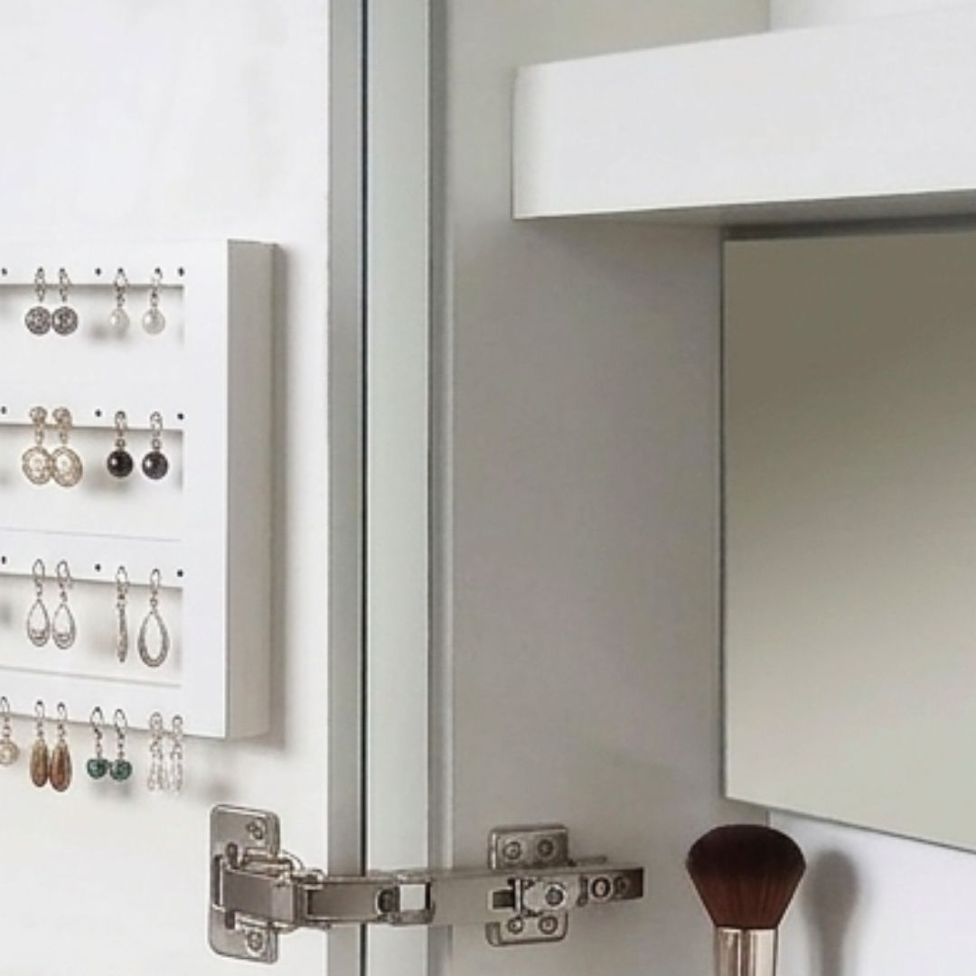 Espejo de tocador de baño con brochas de maquillaje y joyas colgadas en la pared.