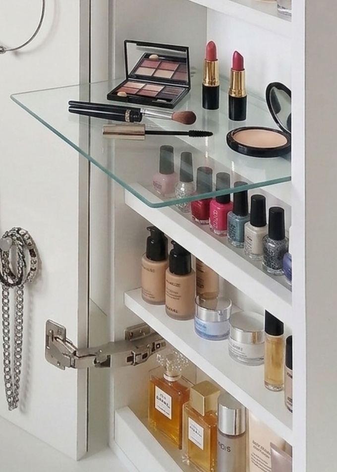 Armario de baño abierto con maquillaje, esmalte de uñas y perfume en estantes de cristal.
