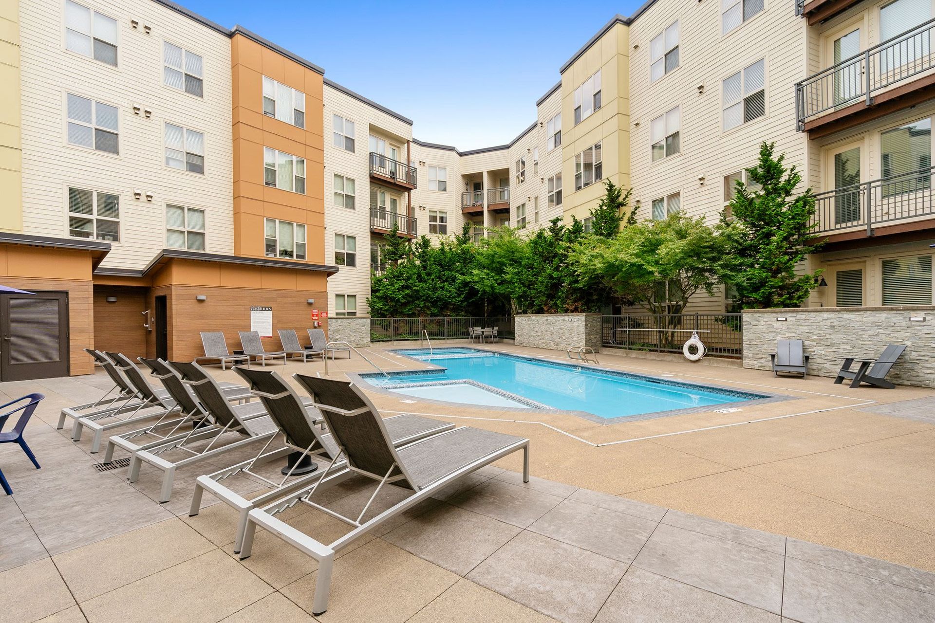 Outdoor pool area at an apartment community with lounge chairs and surrounding buildings.