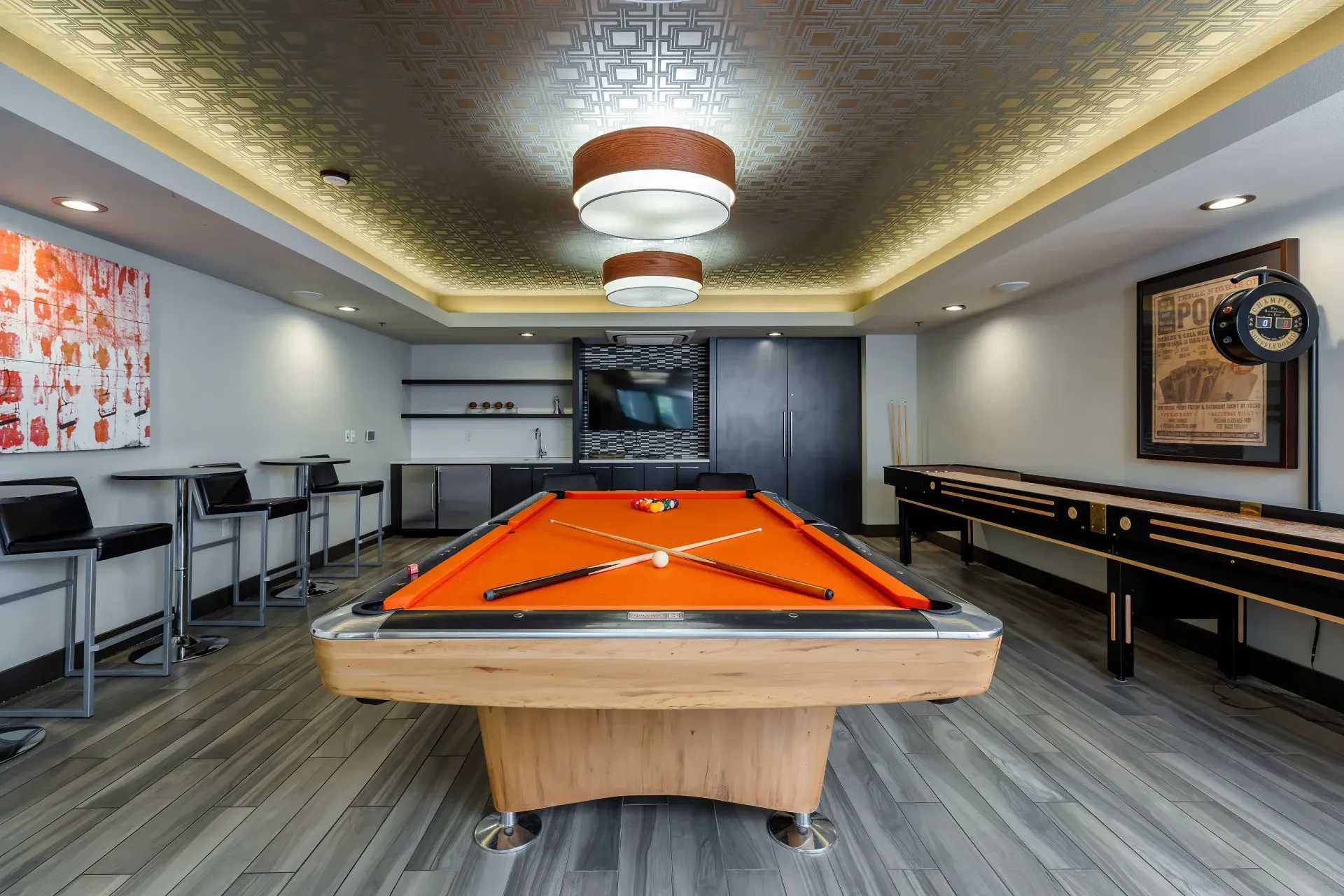 Indoor recreation room with an orange pool table, foosball table, and bar-height seating.