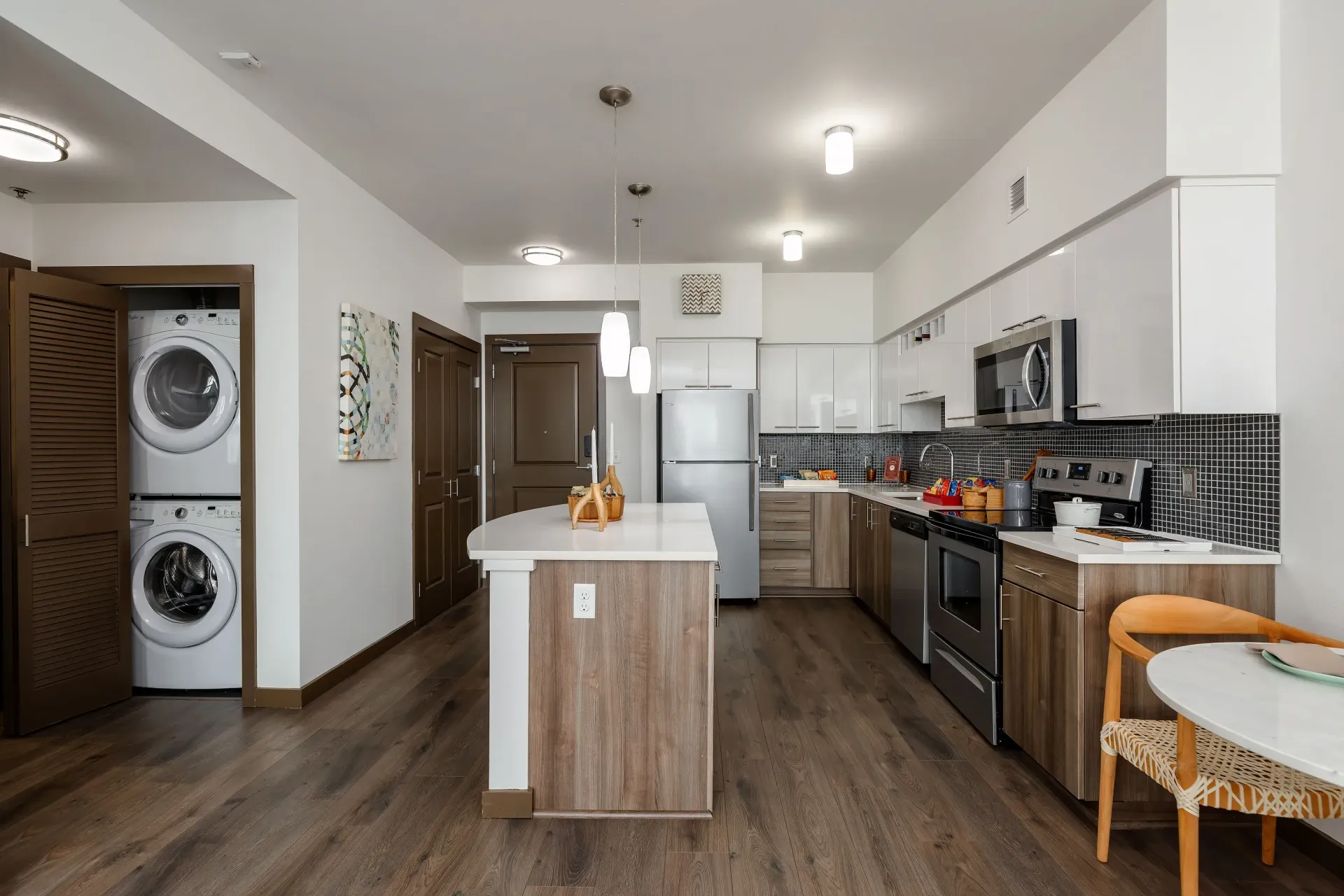 Open-concept kitchen with an island, stainless steel appliances, and a stacked washer/dryer in a closet.