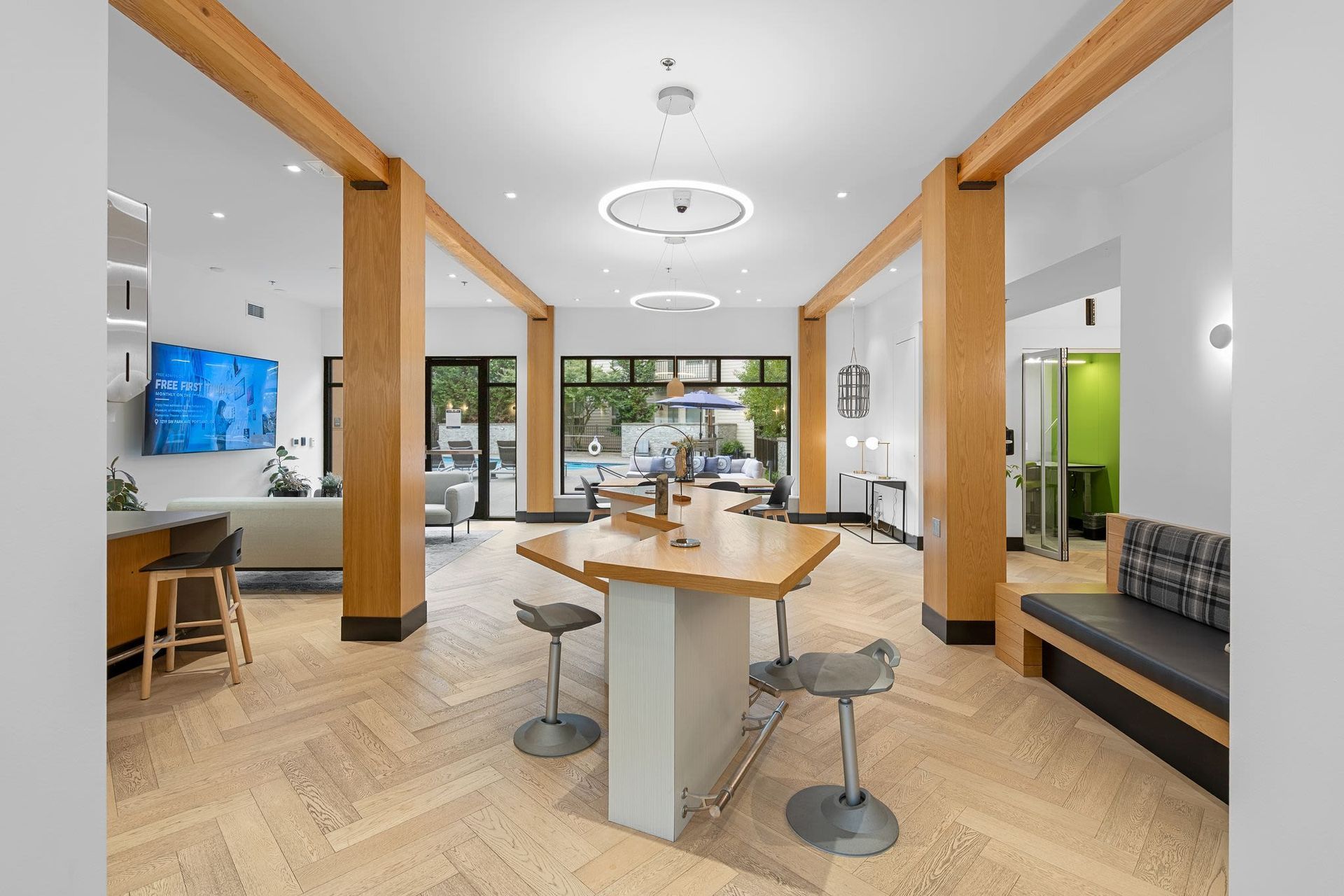 Interior community lounge with a large central wooden table, modern seating, and warm wood beams.