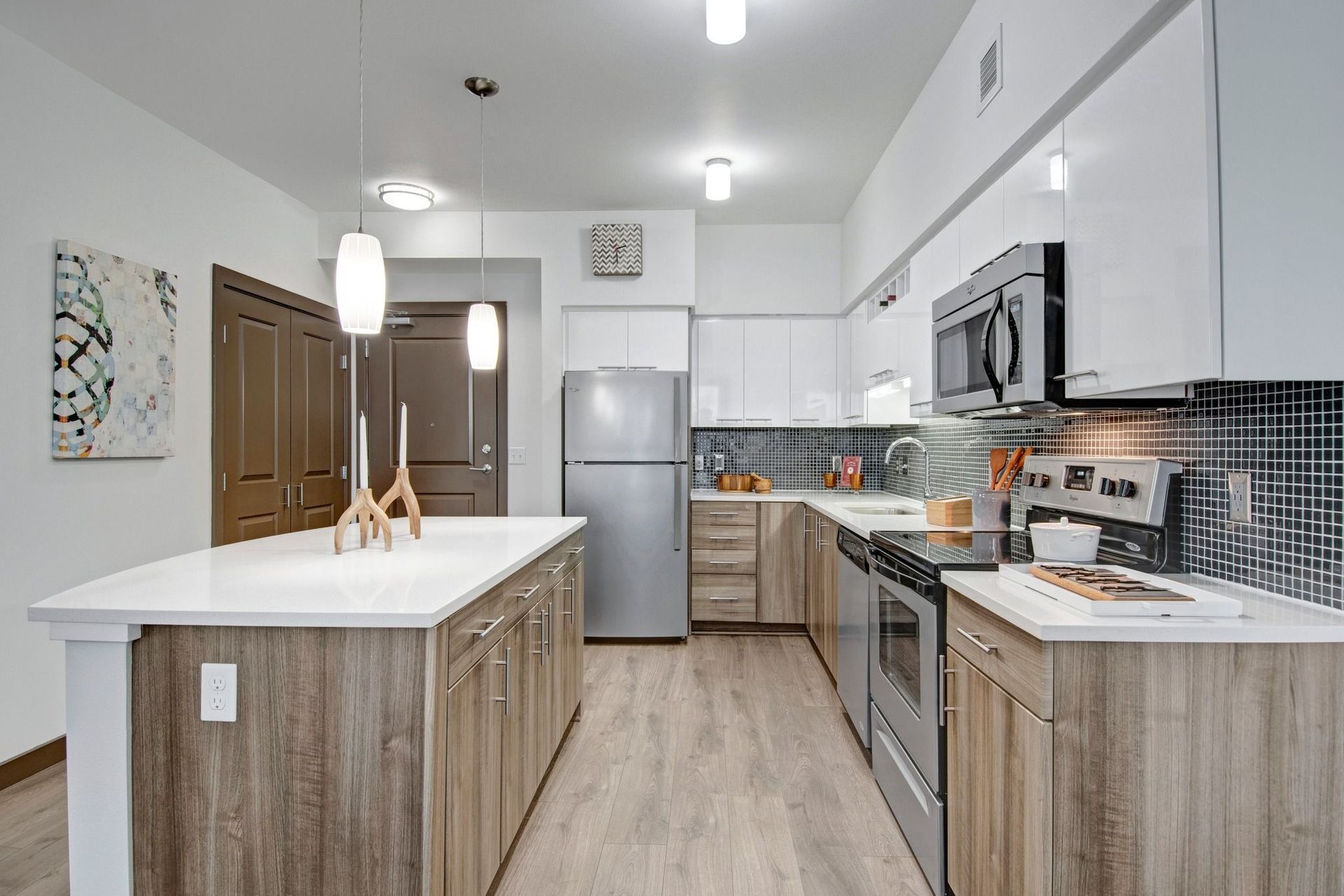 Modern kitchen in apartment with island, white cabinetry, and stainless steel appliances.