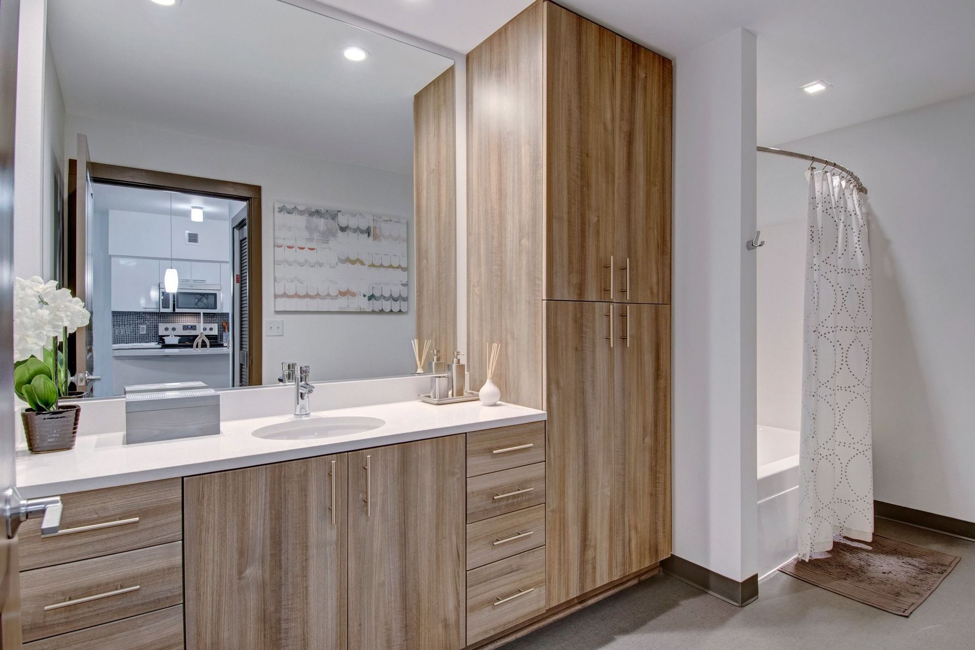 Modern apartment bathroom with wood grain vanity, white countertop, large mirror, and a shower curtain.