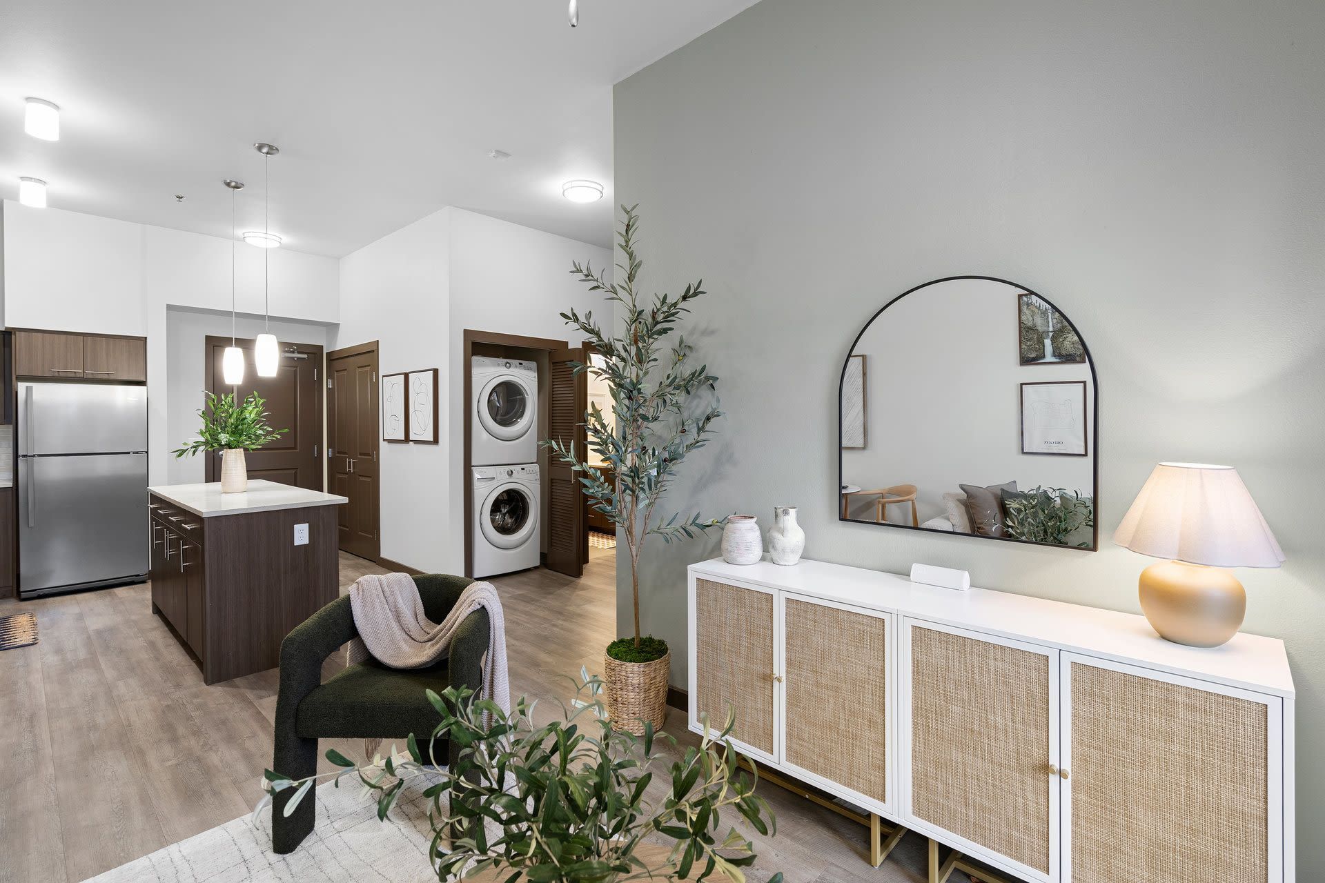 Open-concept living space with kitchen island, stainless steel fridge, and stacked laundry near a doorway.