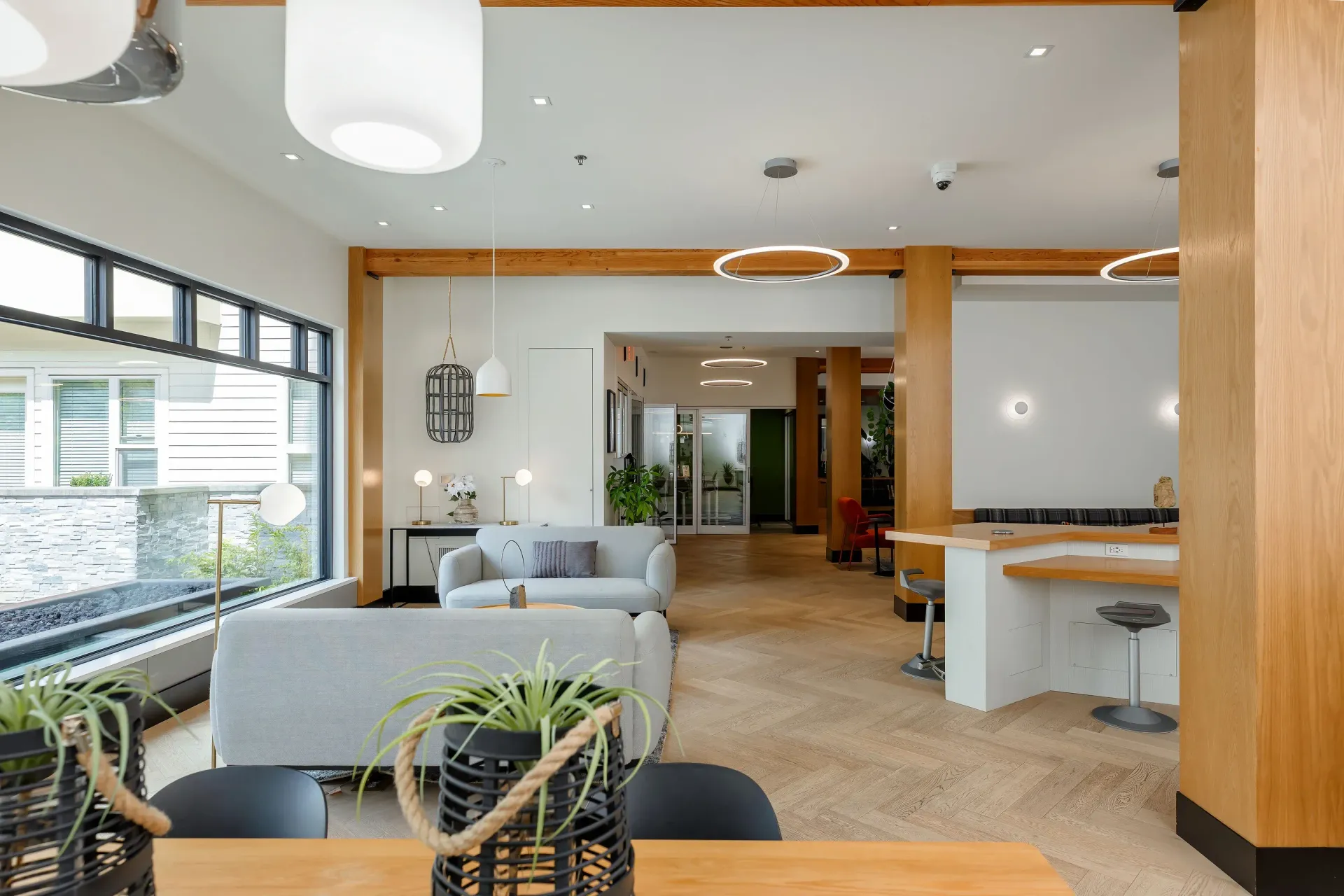 Bright modern community lounge with beige sofas, plants, and large windows.